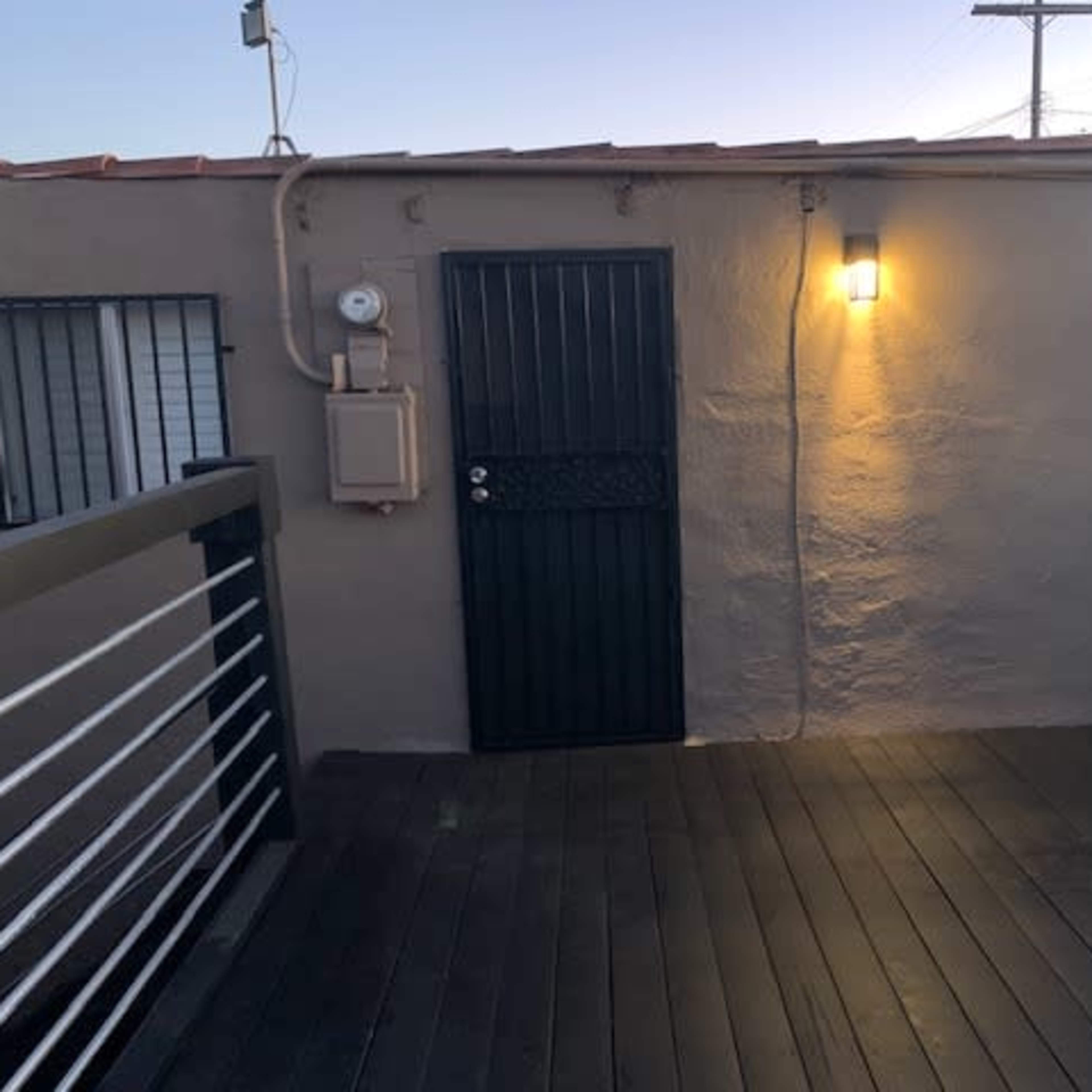 A dark-painted door with two windows on either side, set against a light-colored wall, with a light fixture illuminating the entrance on a wooden deck.