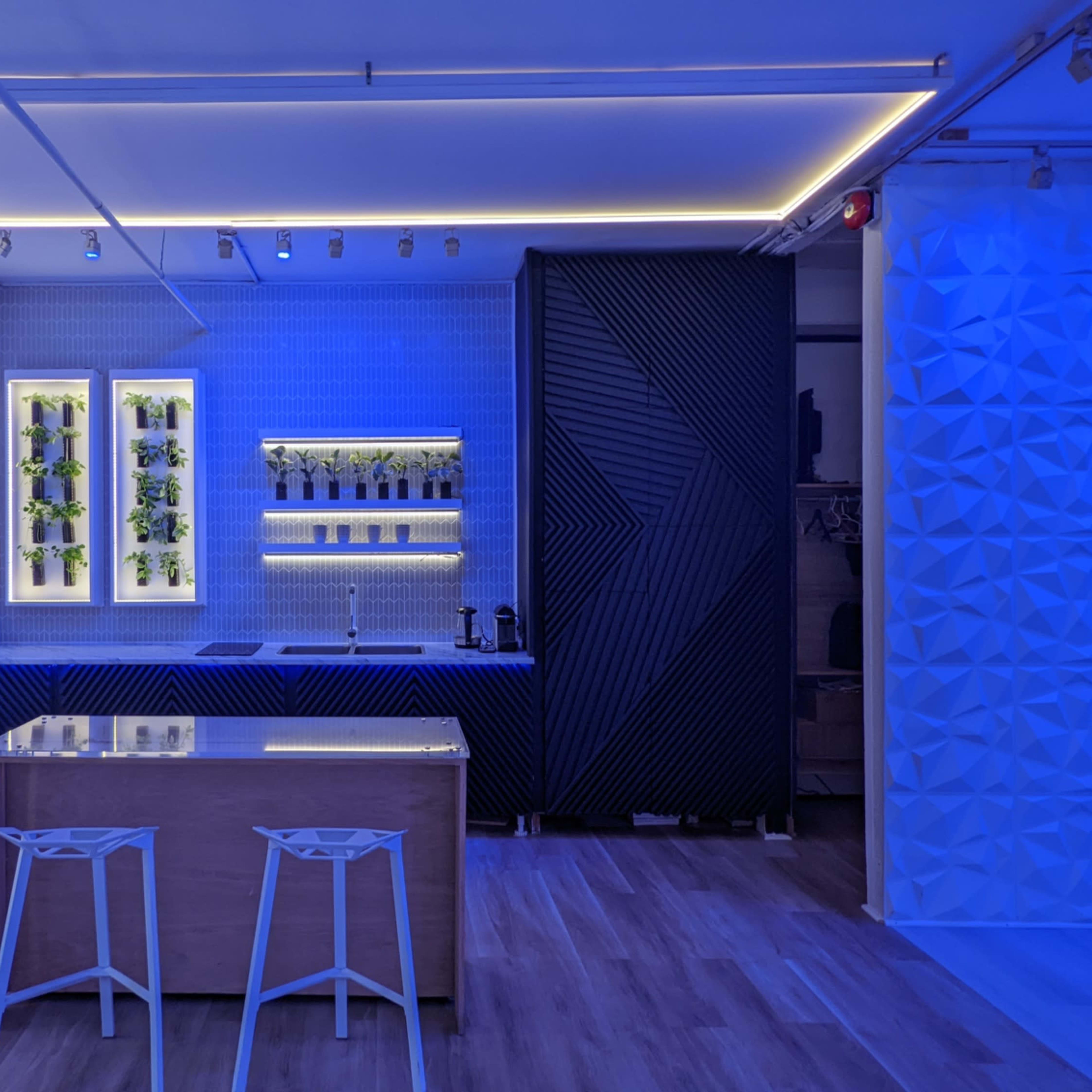 A modern kitchen space illuminated with blue lights, featuring a wooden island and a decorative wall shelf with vases.