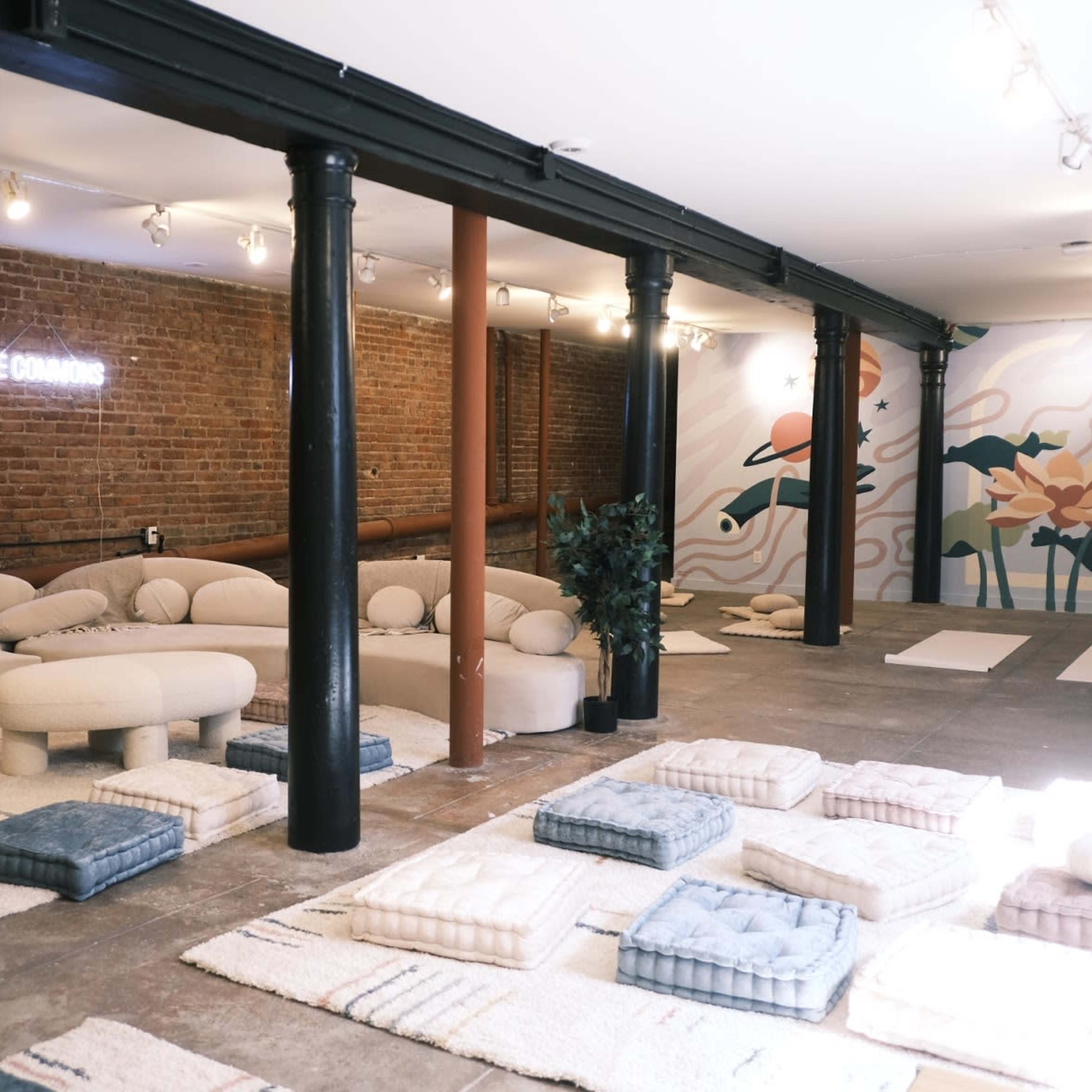 A spacious room with a textured brick wall, featuring soft seating arrangements and cushioned mats on a concrete floor.