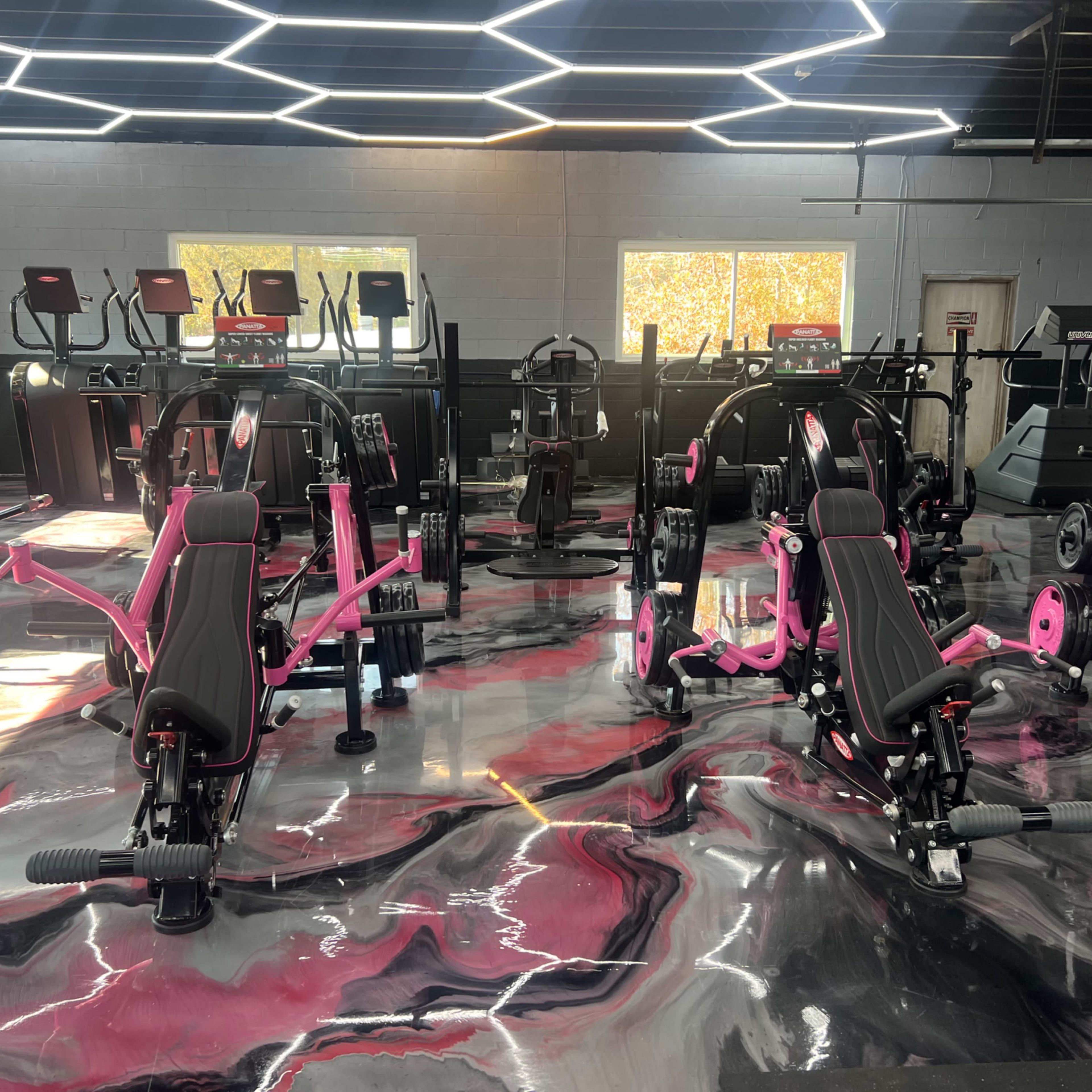 A modern gym interior featuring various exercise machines with black and pink designs on a glossy, marble-patterned floor.