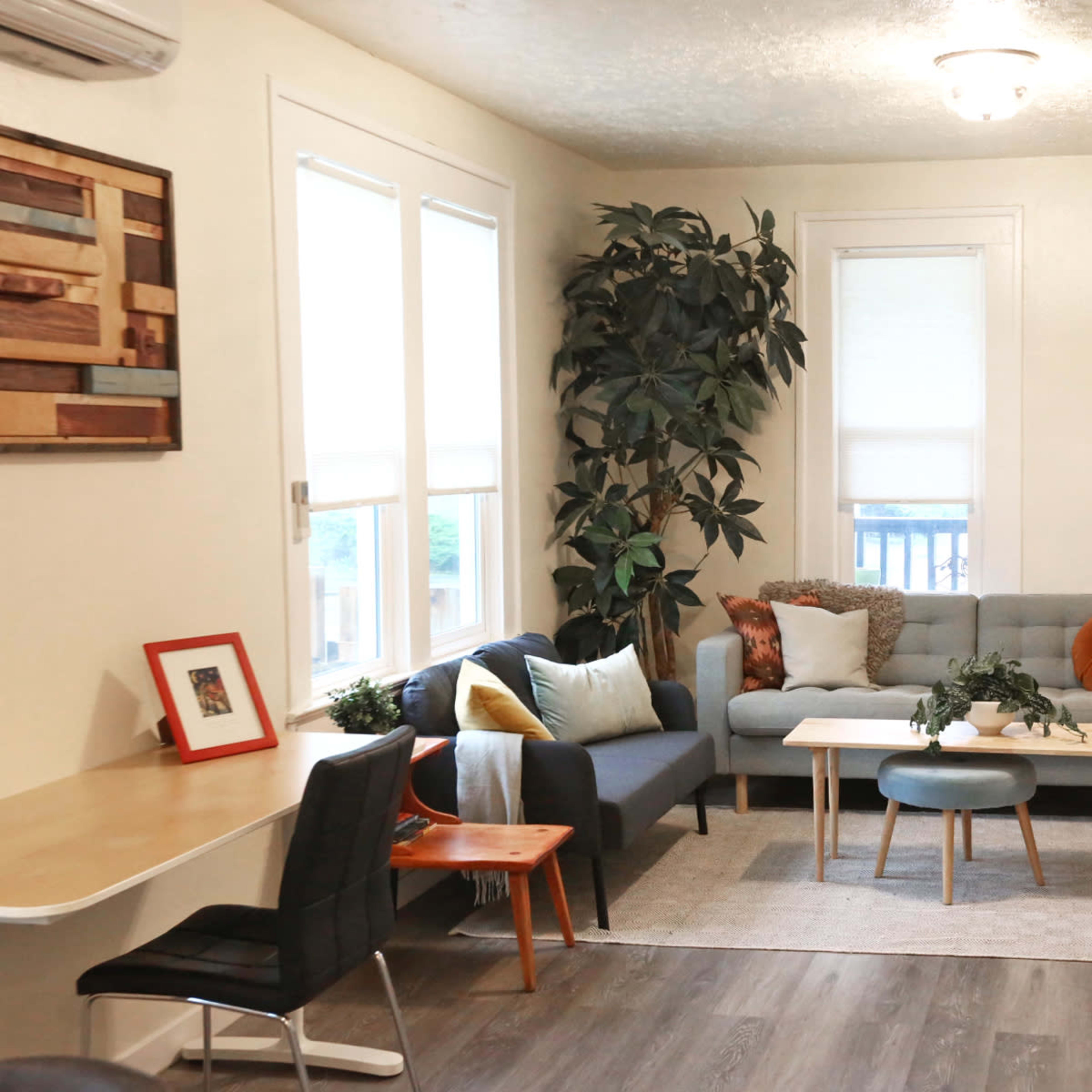 A living room with a gray sofa, a couple of wooden tables, and decorative plants by the window.