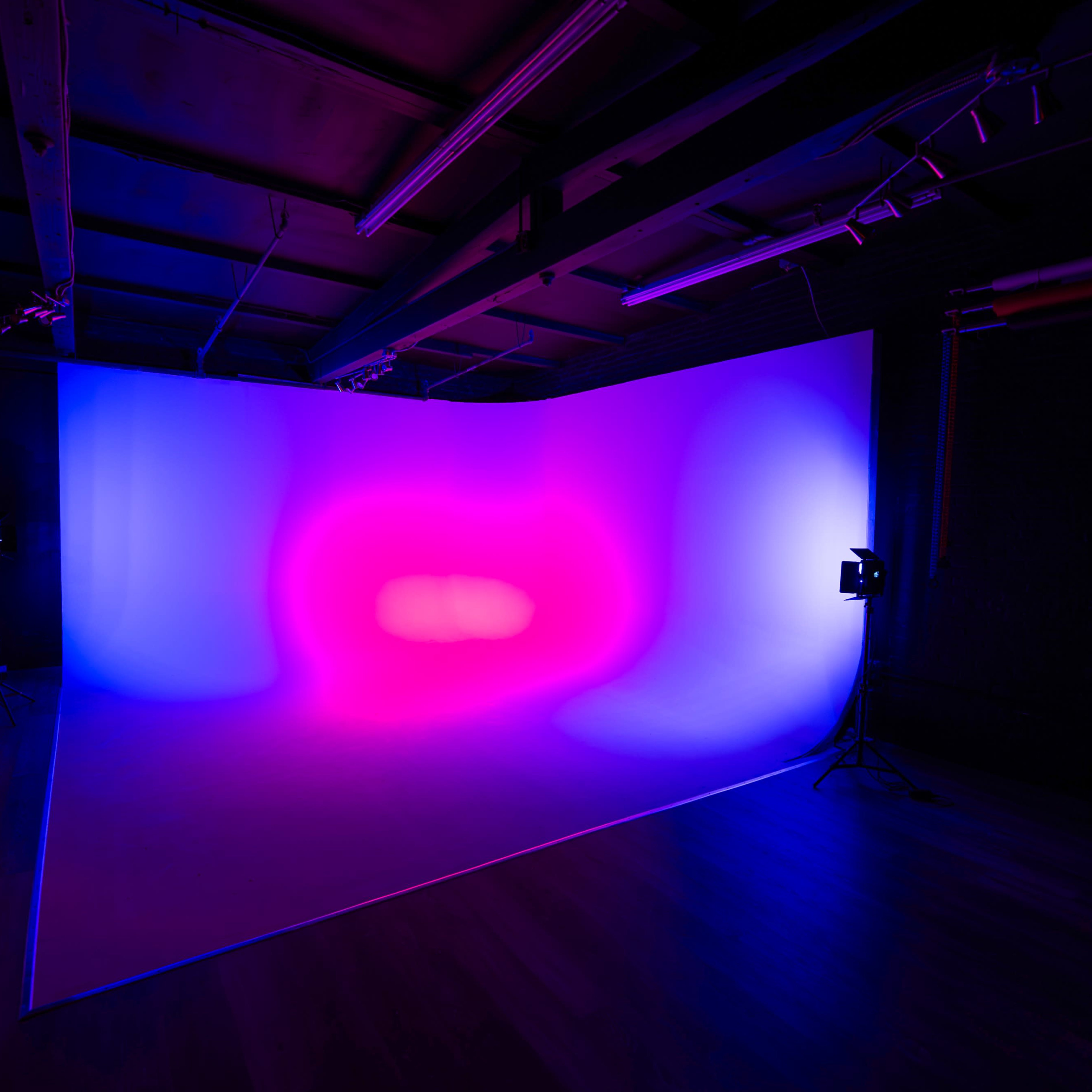 A photography studio features a gradient backdrop illuminated by vibrant purple and blue lights.