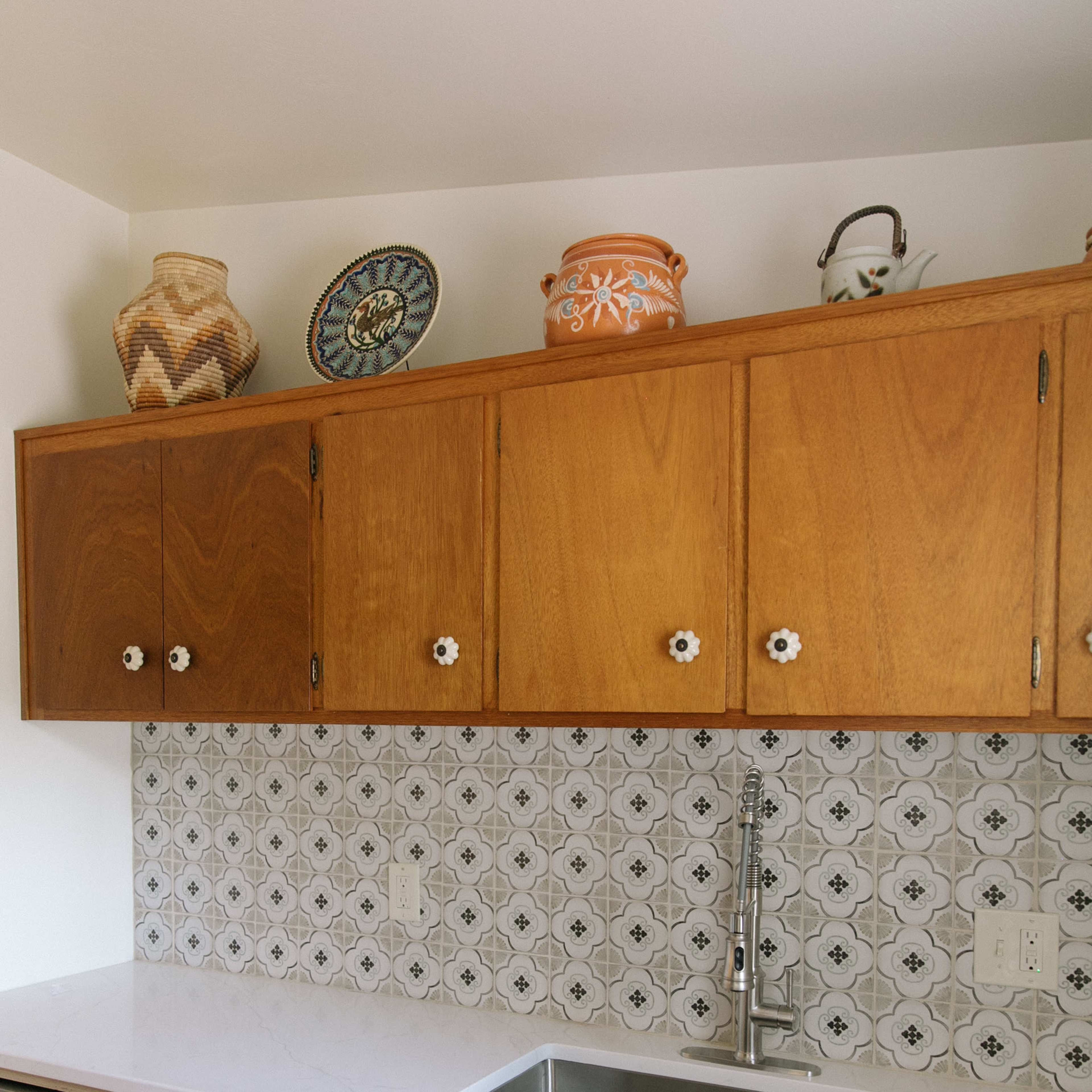 The kitchen features wooden cabinets with ceramic handles, a stainless steel sink, and decorative pottery on the shelves above a tiled backsplash.