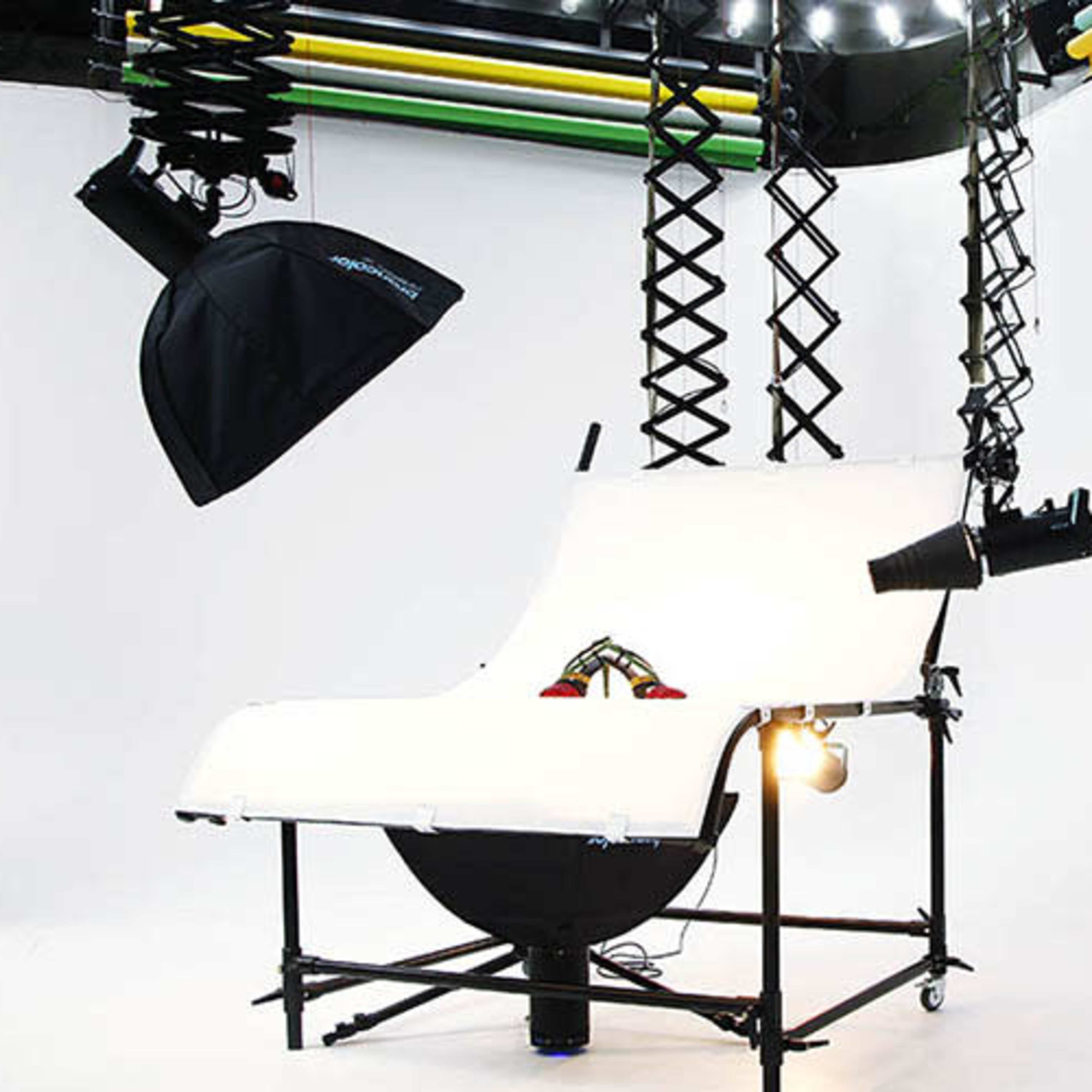A photography setup with white backdrop, lighting equipment, and a raised platform on a wheeled frame.