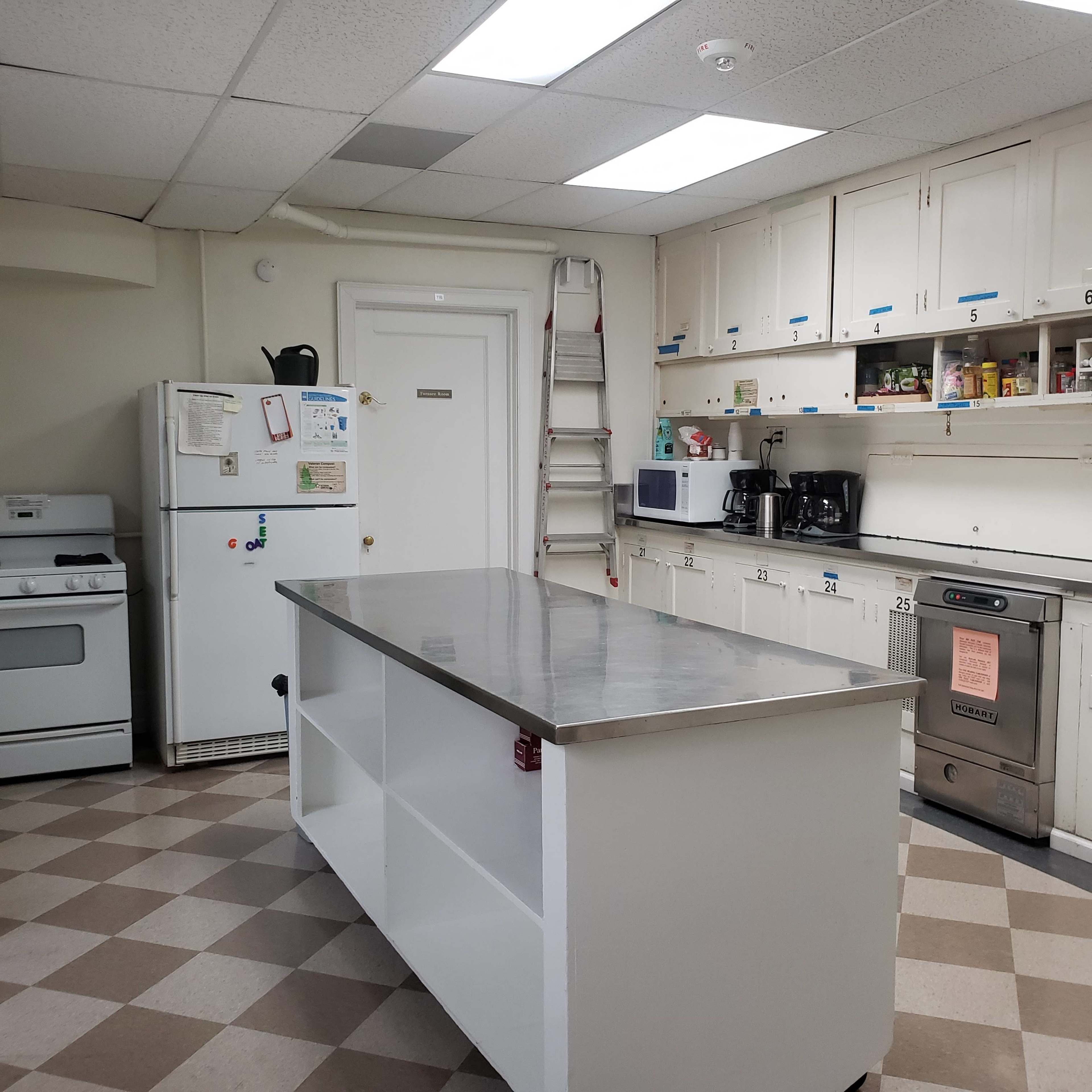 A kitchen with a central island, a refrigerator, an oven, a microwave, coffee makers, and cabinets lining the walls.