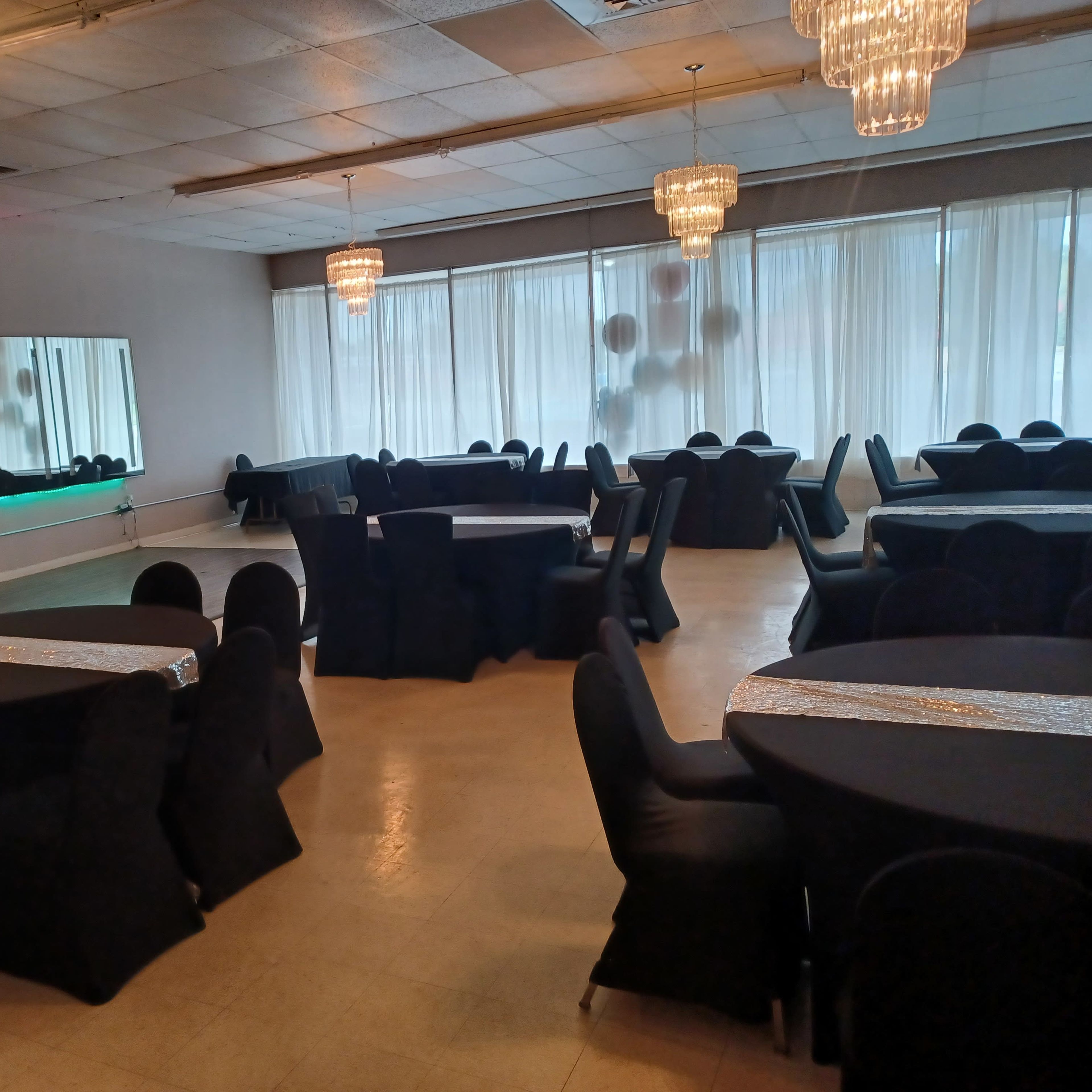 A spacious banquet hall with round tables covered in black cloth and elegant chandeliers hanging from the ceiling.