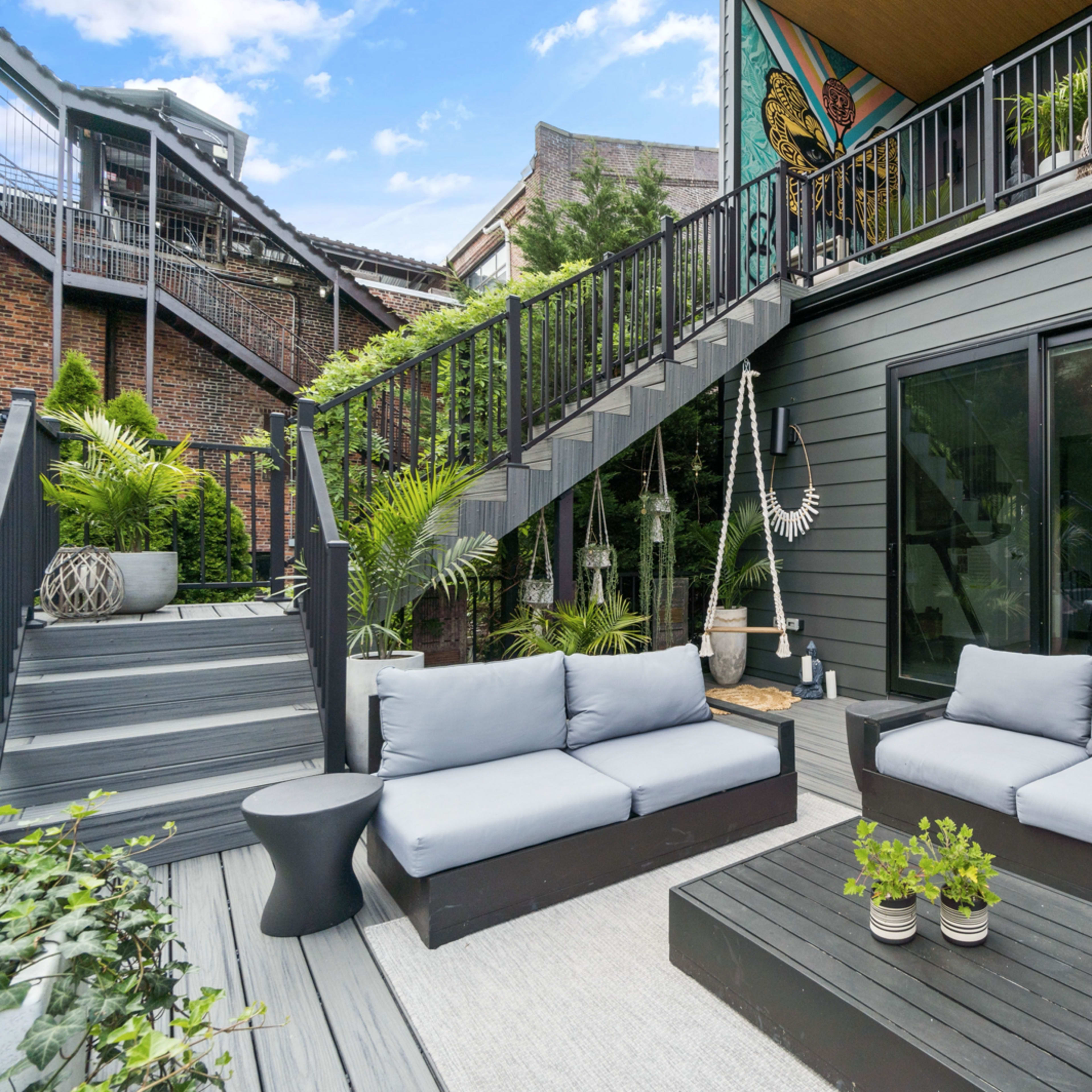 A modern outdoor patio with gray seating, a low coffee table, and greenery surrounding a well-defined space.