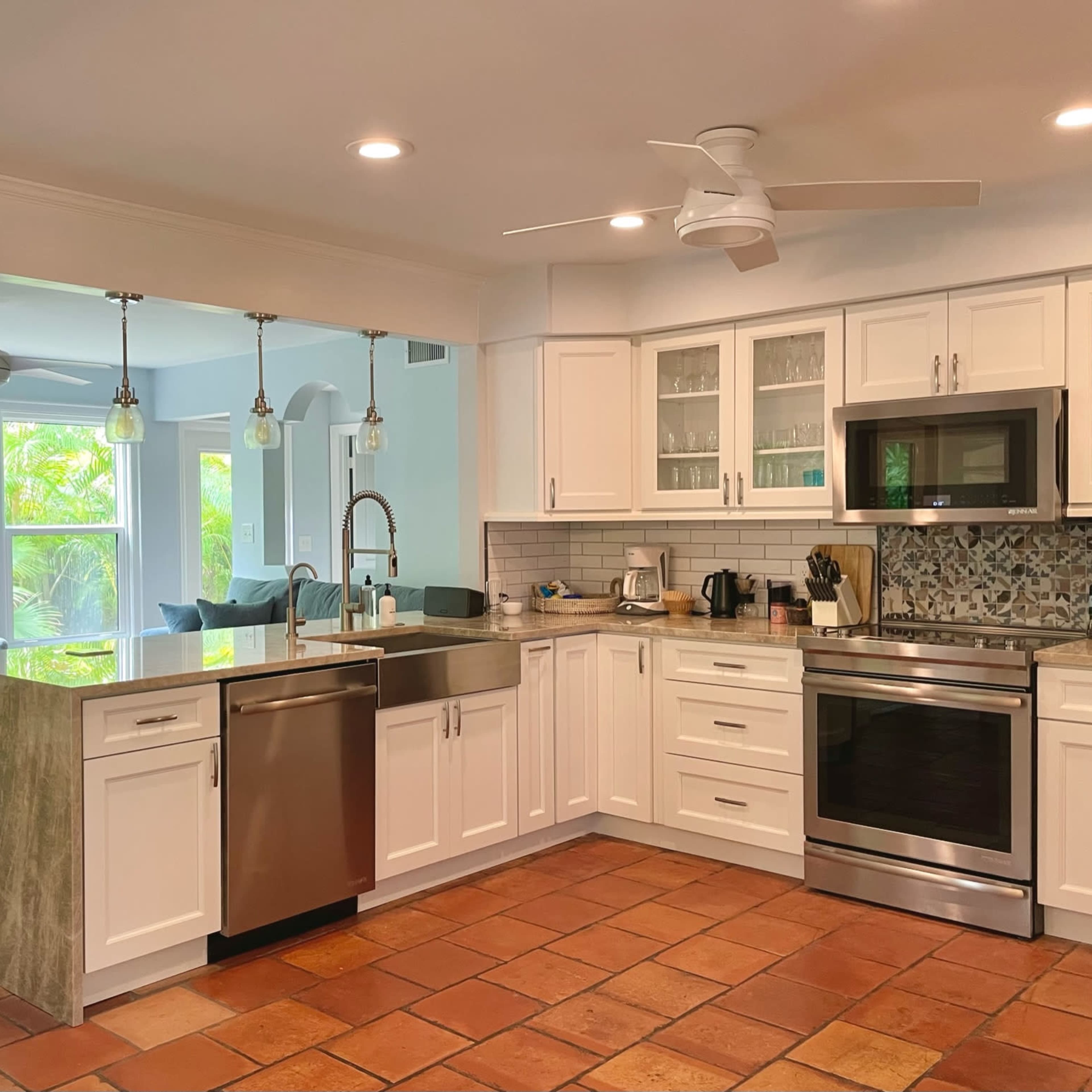 A modern kitchen features white cabinetry, stainless steel appliances, and a spacious island with a gray countertop, connected to a cozy seating area filled with natural light.