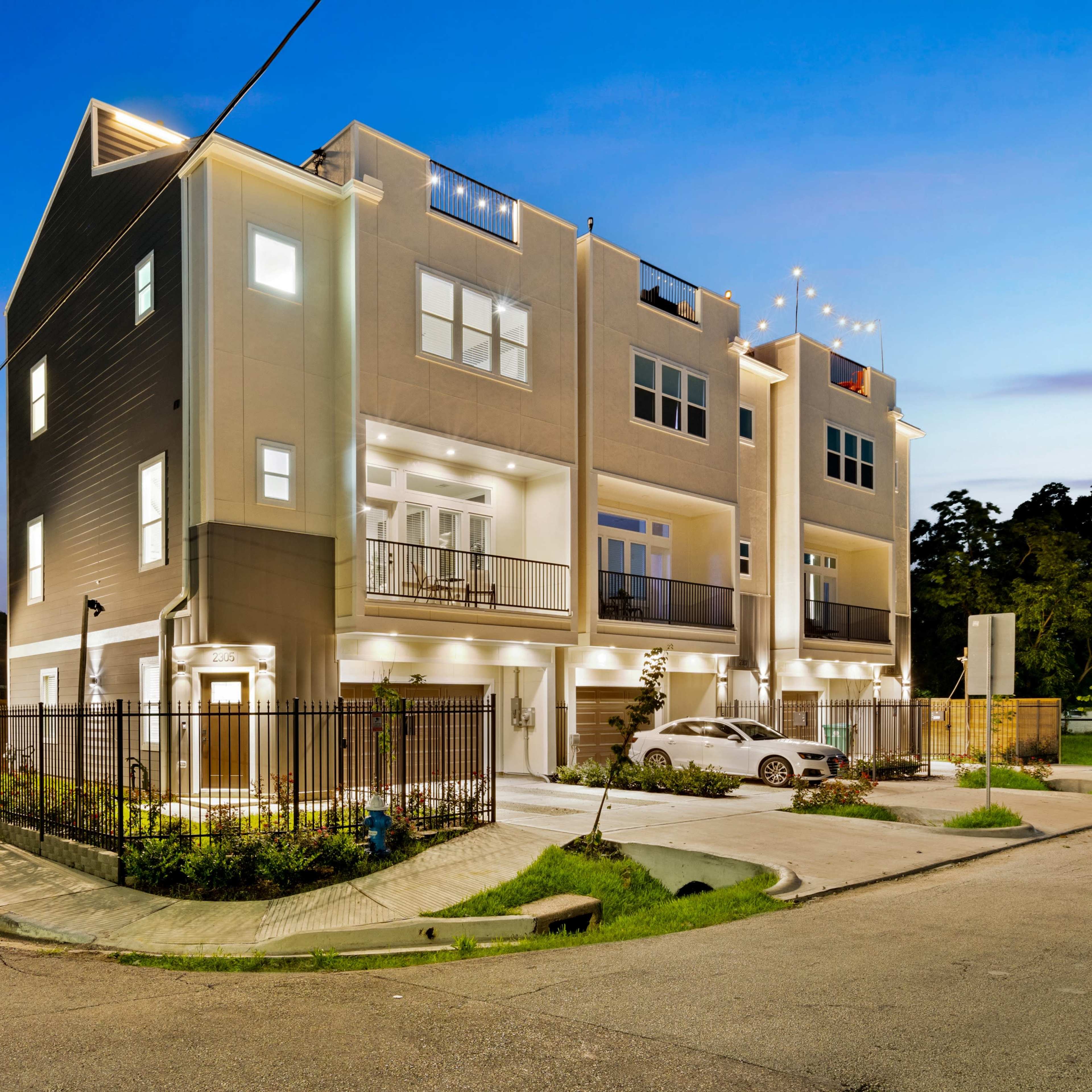 A modern multi-story house is illuminated at dusk, showcasing its sleek architecture and outdoor lighting.