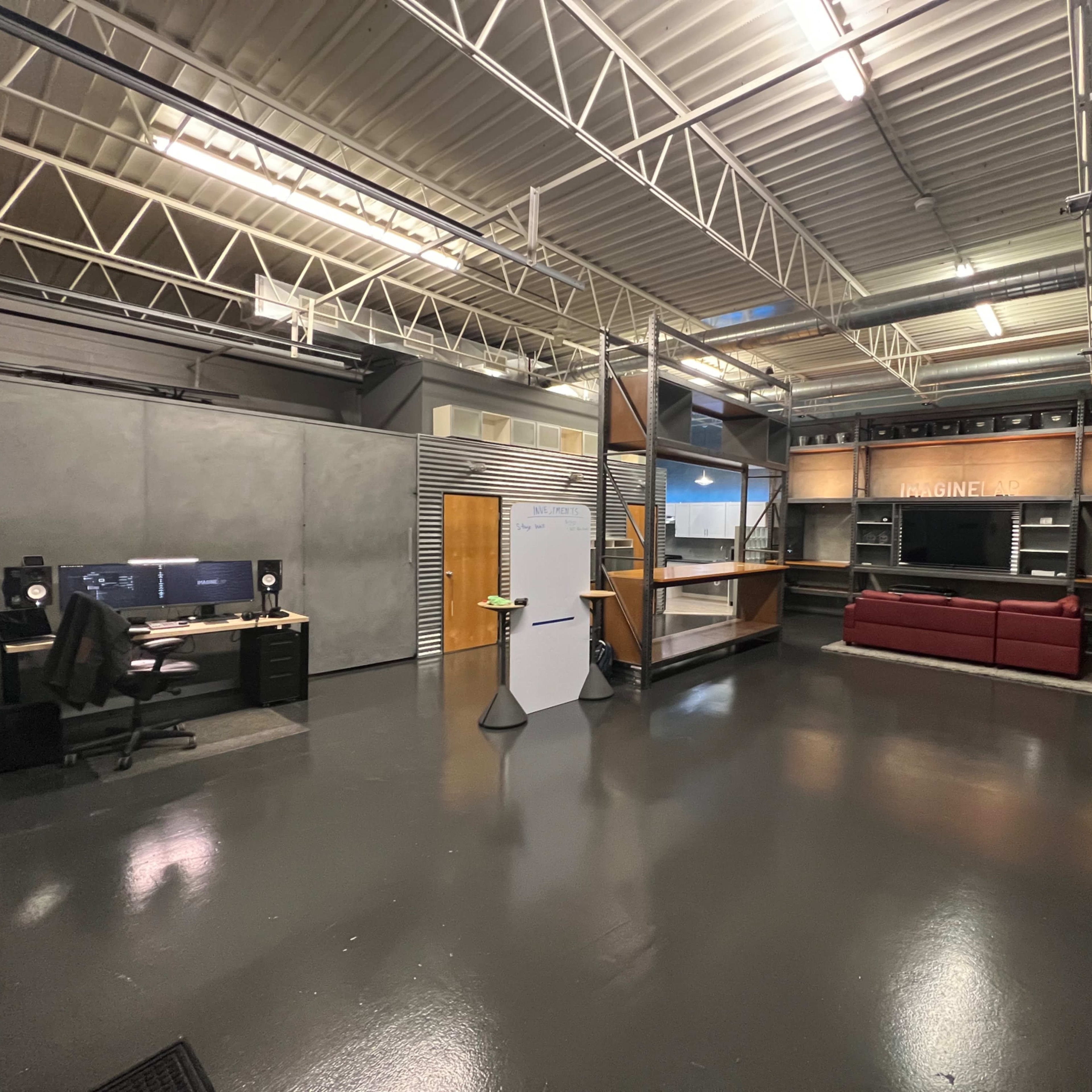 A spacious office interior with a workstation, a whiteboard, and a seating area featuring a red couch against a backdrop of shelving.