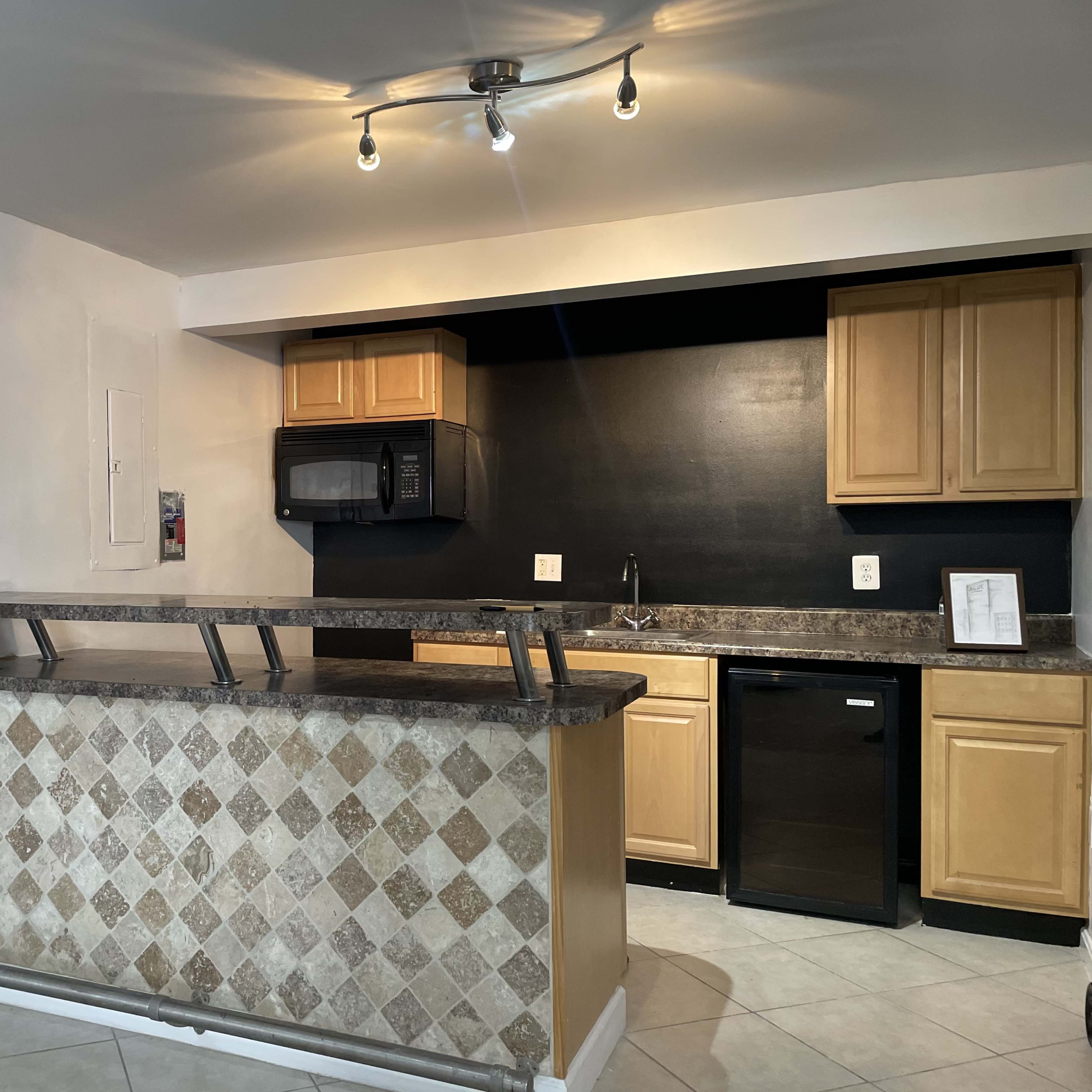 This image shows a kitchen area featuring a bar with a tiled front, wooden cabinets, and appliances including a microwave and a refrigerator.
