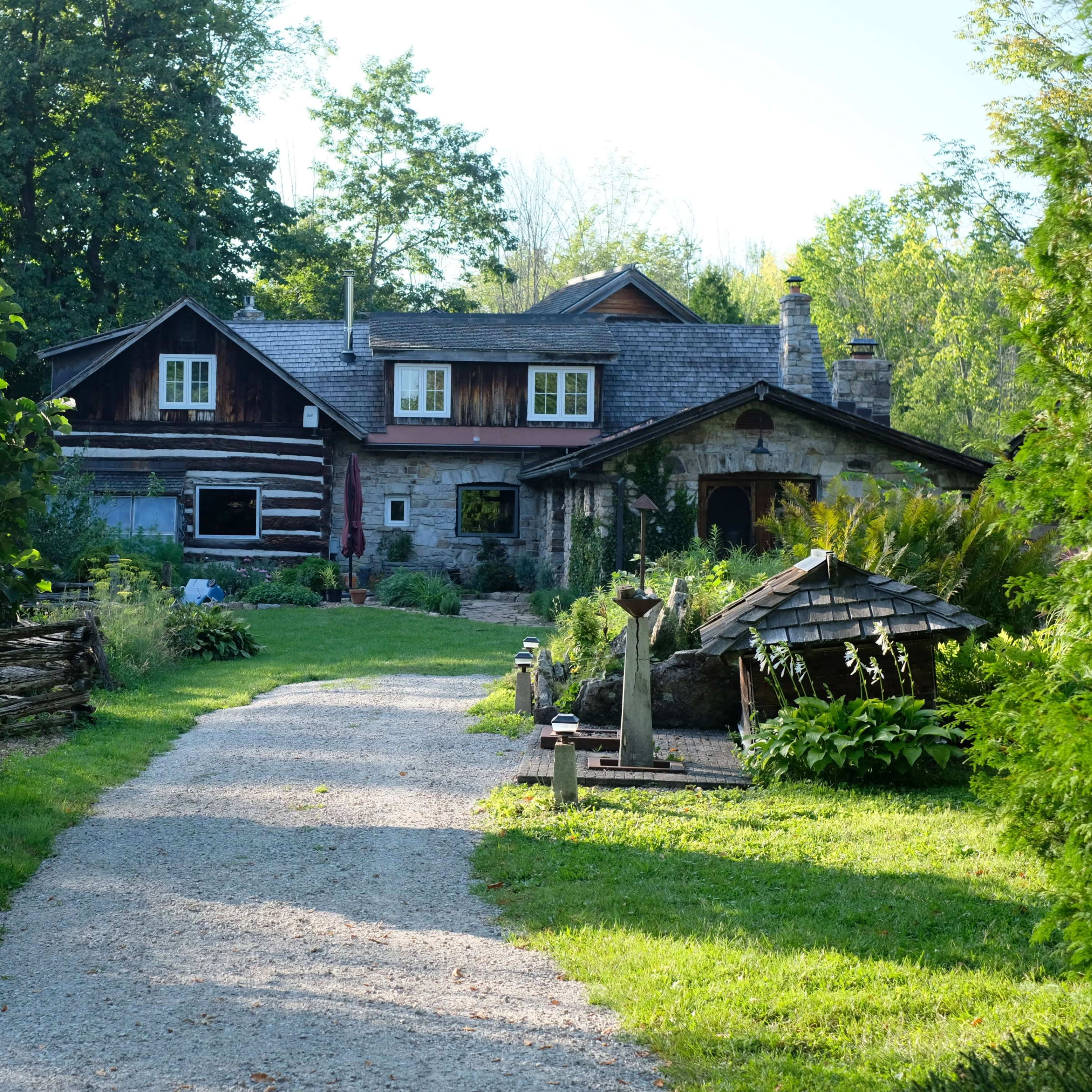 A gravel pathway leads to a rustic house surrounded by greenery and gardens.