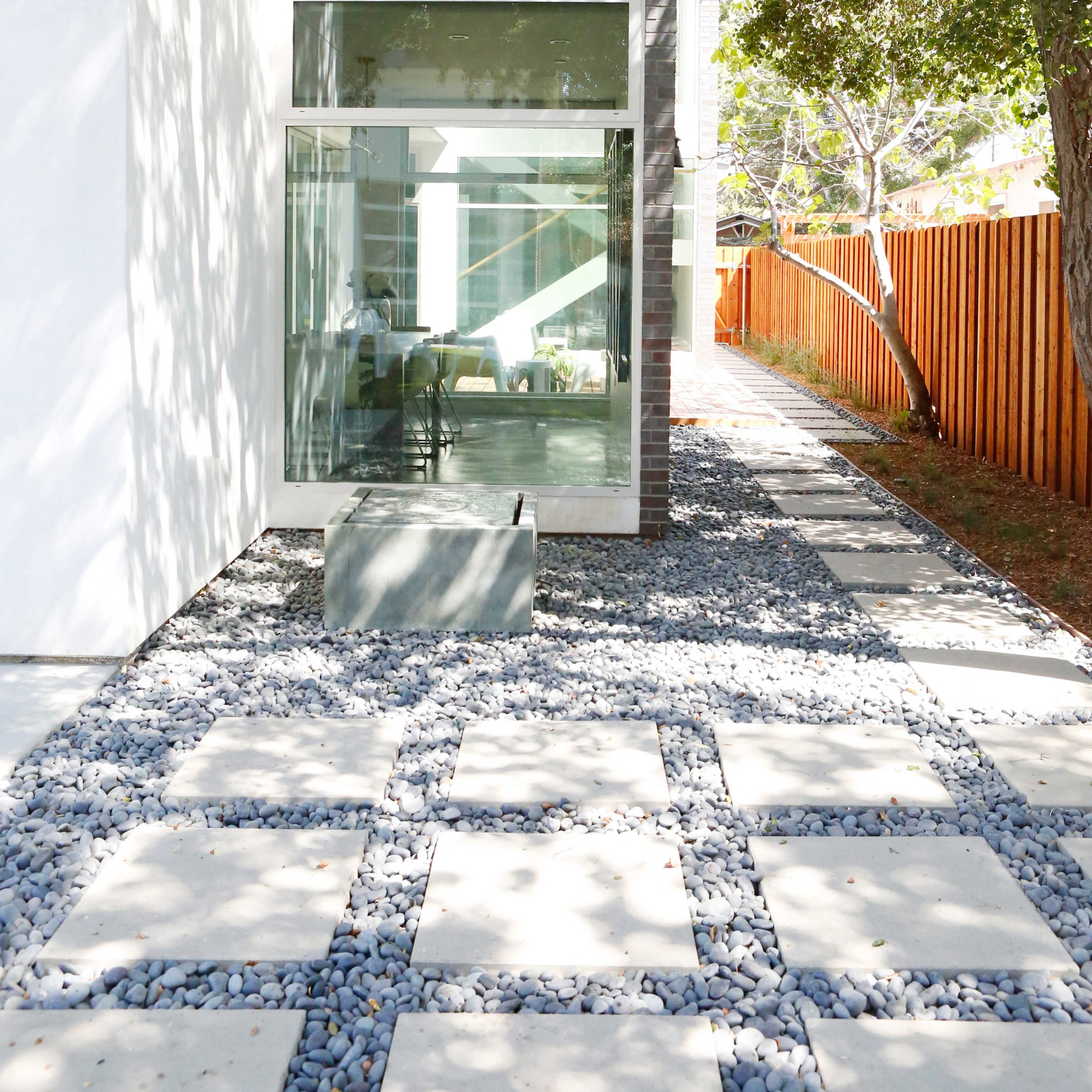 A modern home features a pathway of stone pavers surrounded by gravel, leading to large glass doors with a view of an interior space.