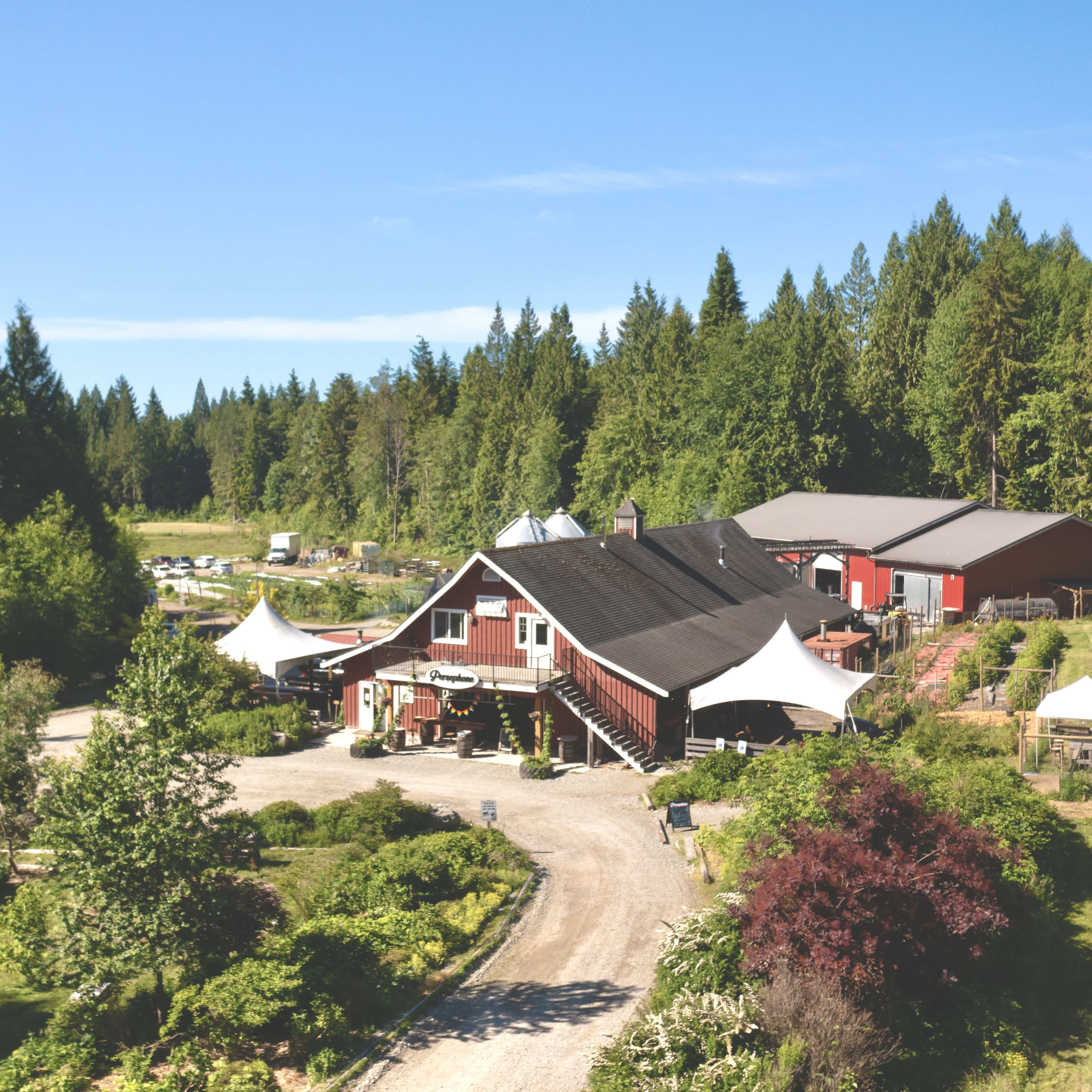 A red barn-style building surrounded by gardens and trees, with white tents set up outside.