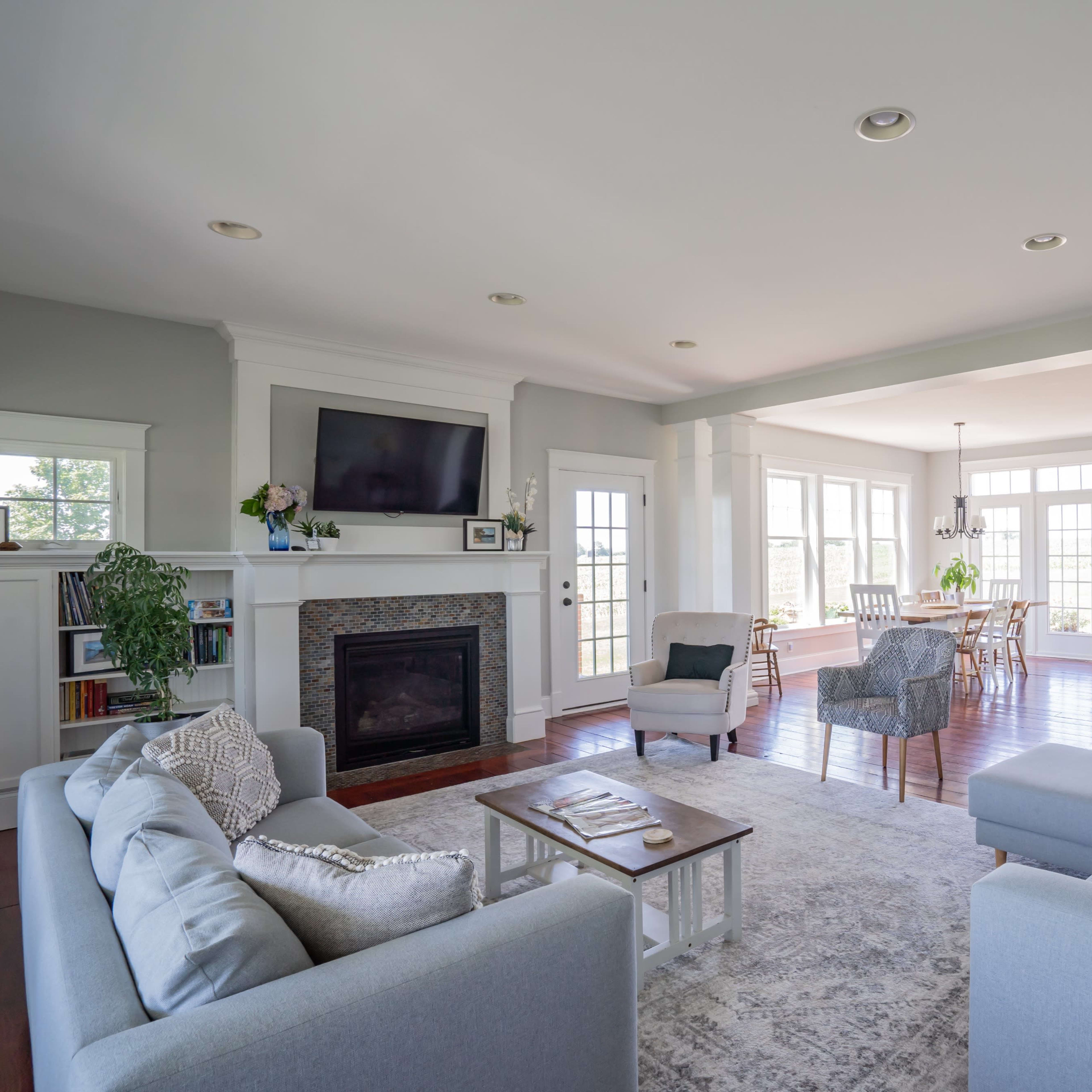 A modern living room with a fireplace, two sofas, and large windows allowing natural light to fill the space.
