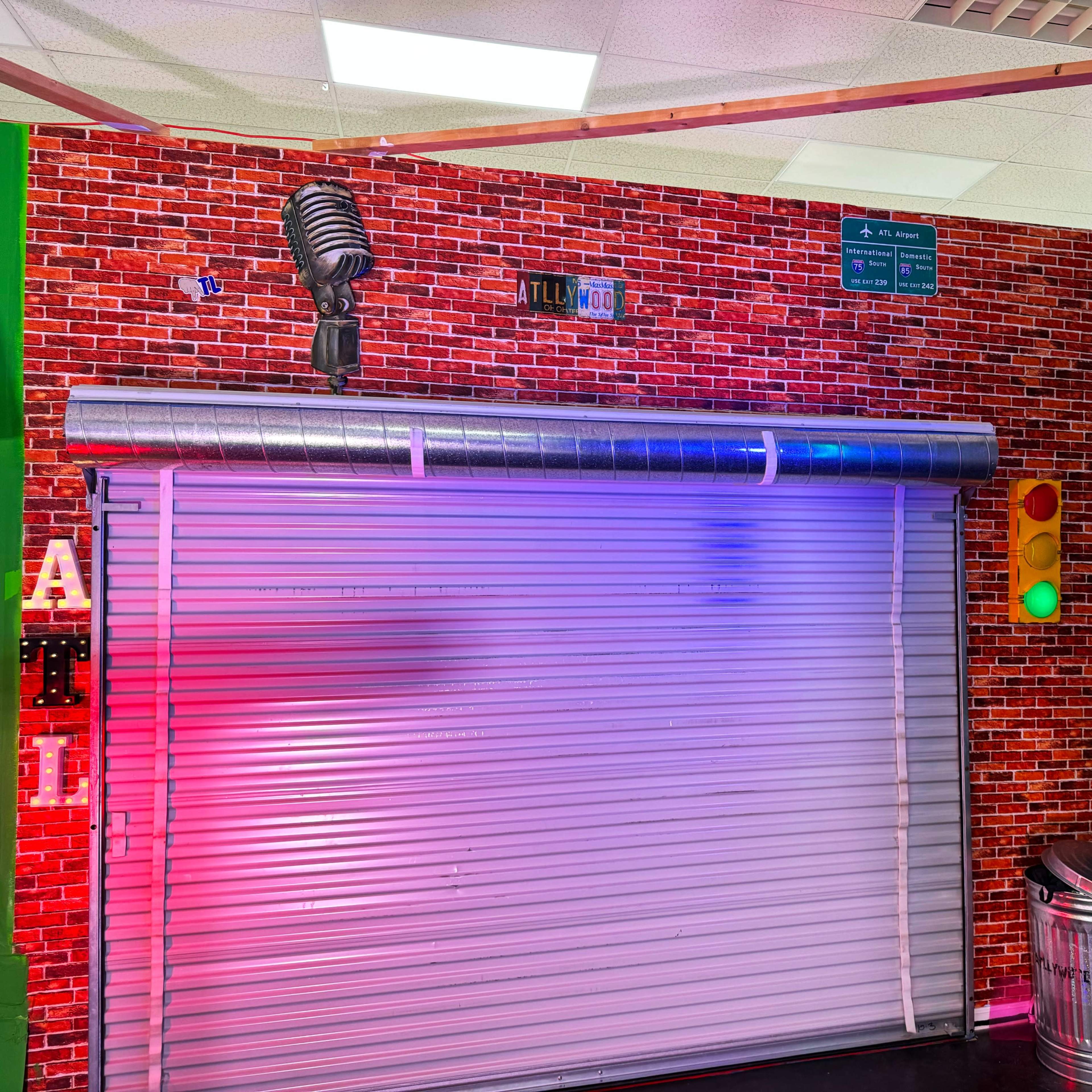 The scene features a brick wall backdrop with a vintage microphone and a rolled-down metal shutter, illuminated by colorful lights.