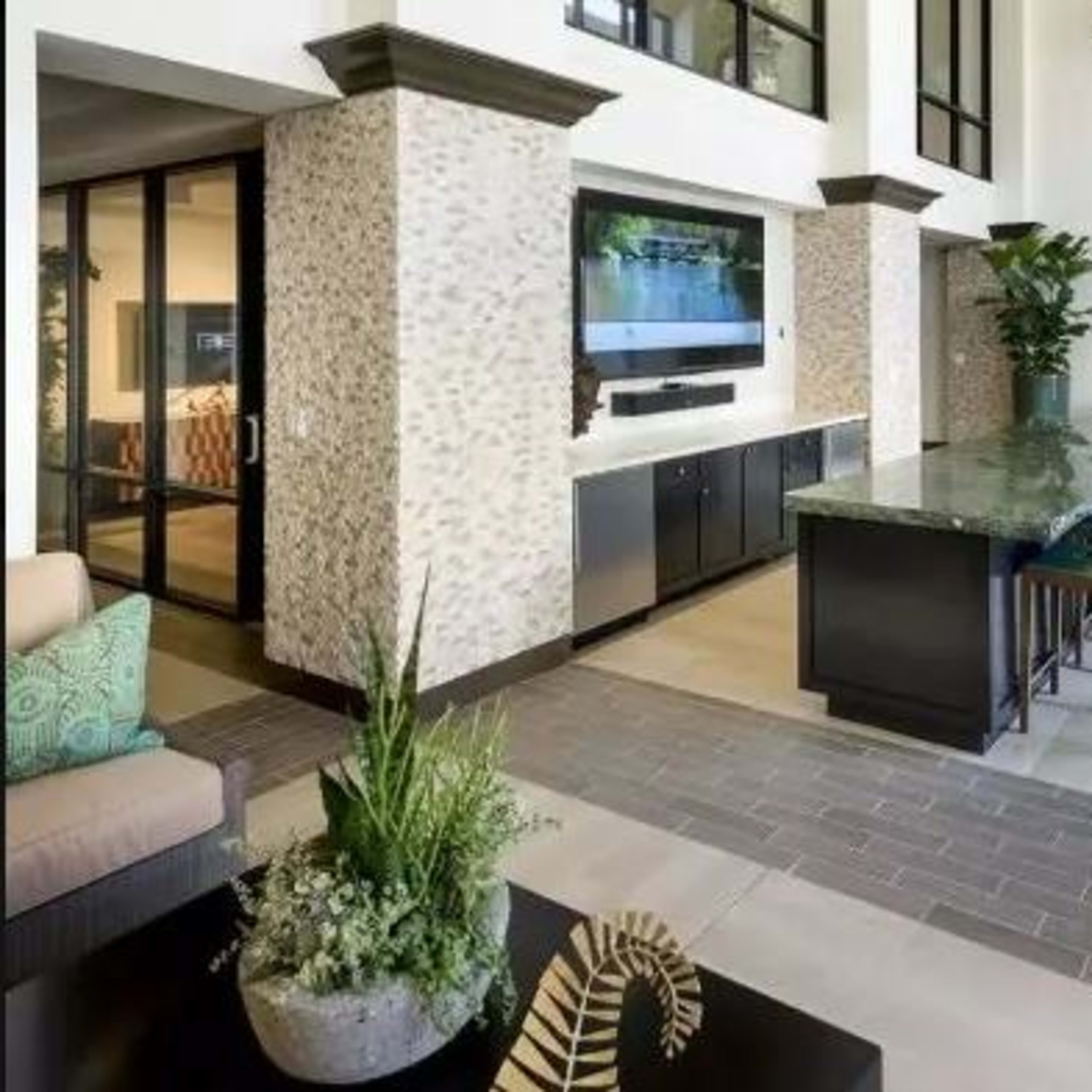 A modern open-concept lobby area featuring a long countertop with bar seating, indoor plants, and large windows.