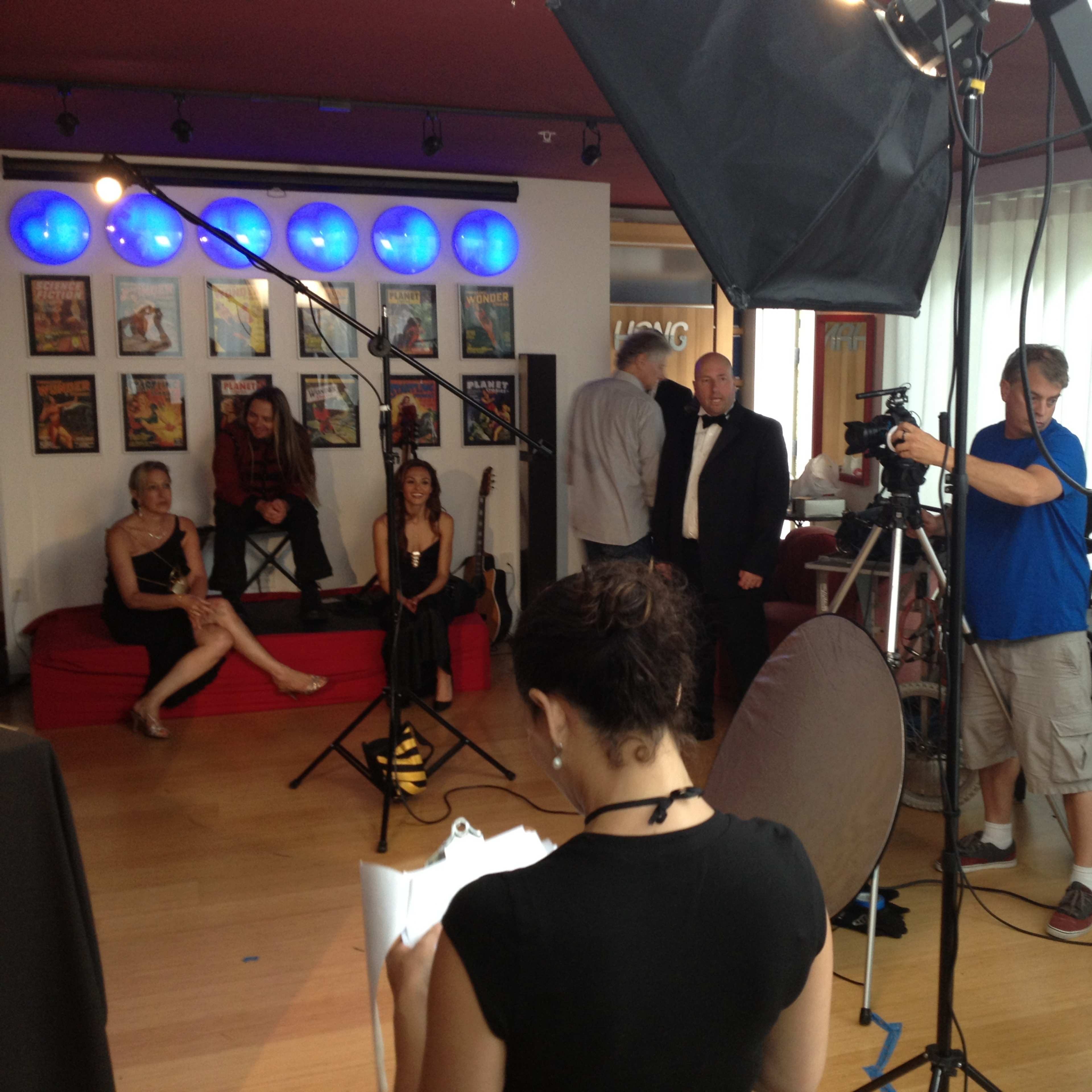 A photo shoot is taking place in a brightly lit studio with several people posing and others setting up equipment.