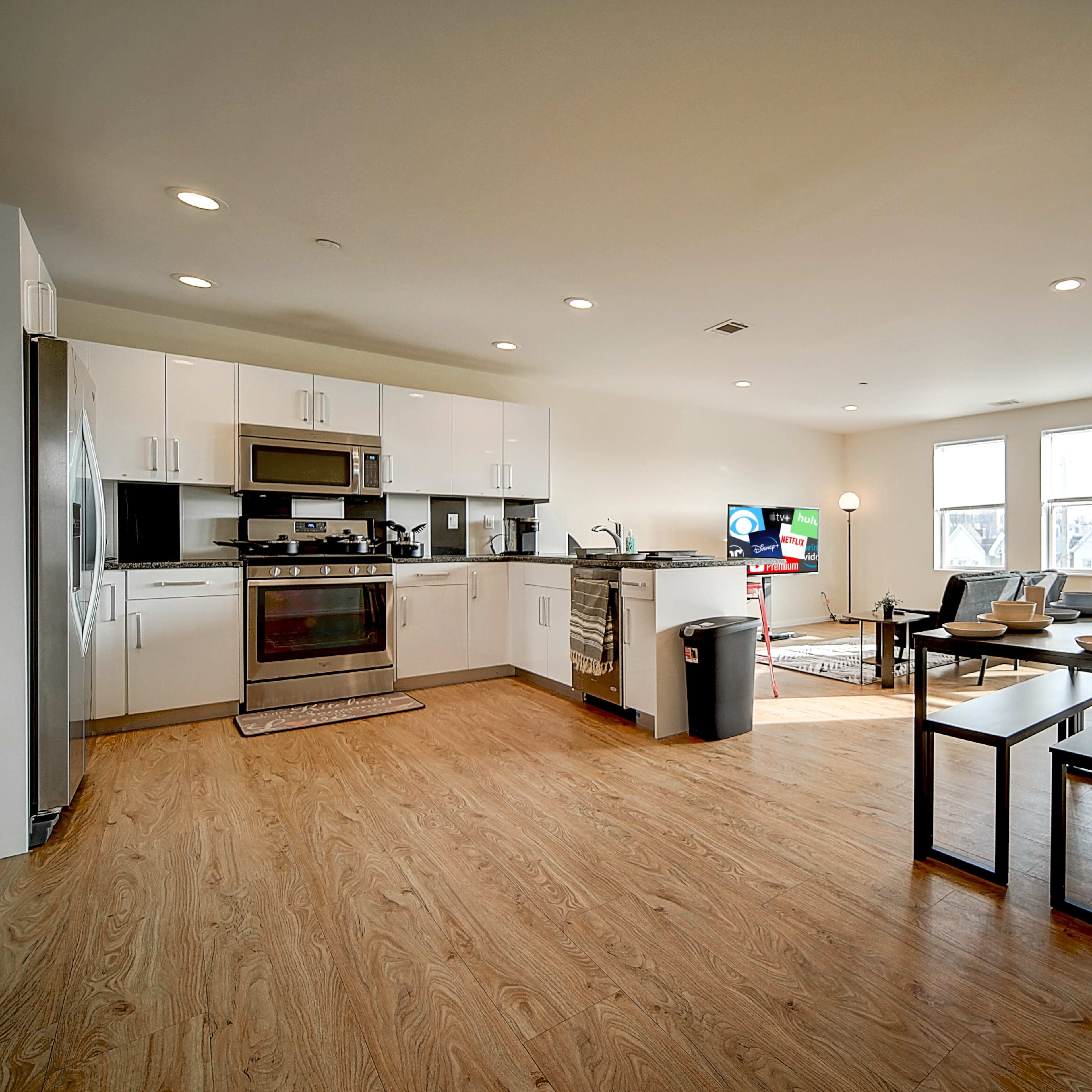 A modern, open-concept kitchen and living area with a dining table and large windows allowing natural light.