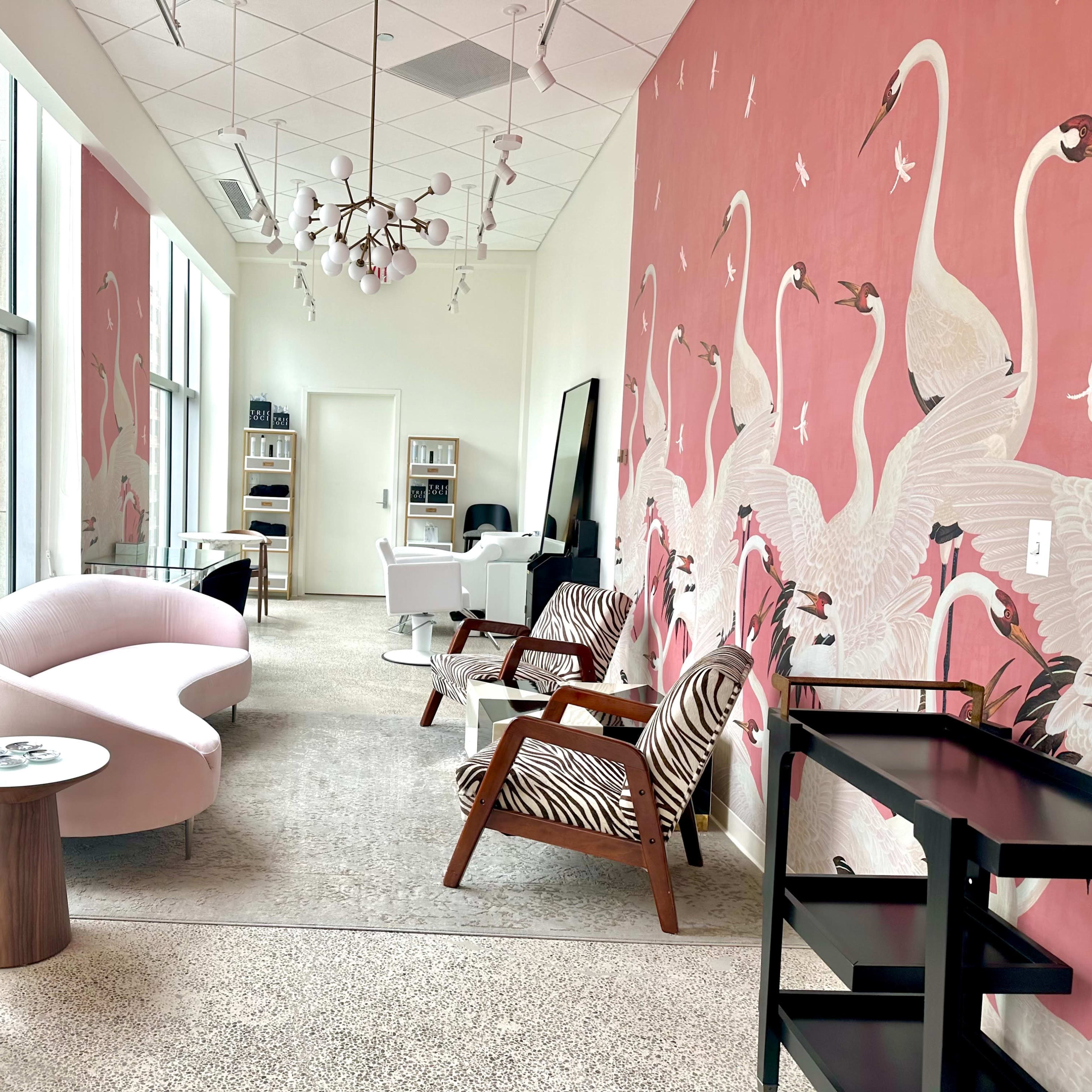 A modern waiting area featuring pink walls adorned with flamingo murals, contemporary furniture including a curved sofa, zebra-patterned chairs, and a large mirror.