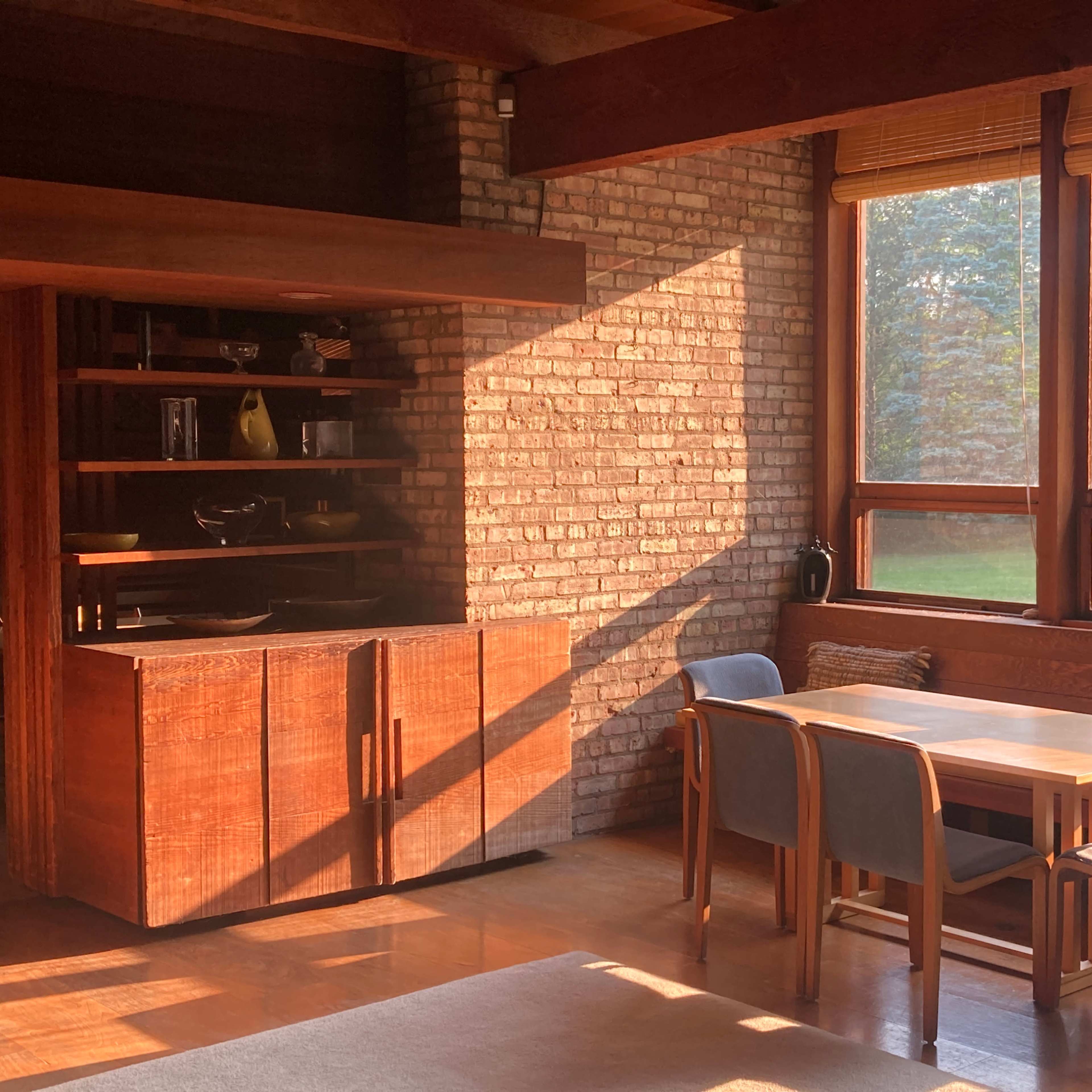 A cozy dining area with a wooden table and chairs, adjacent to a brick wall and large windows that let in natural light.