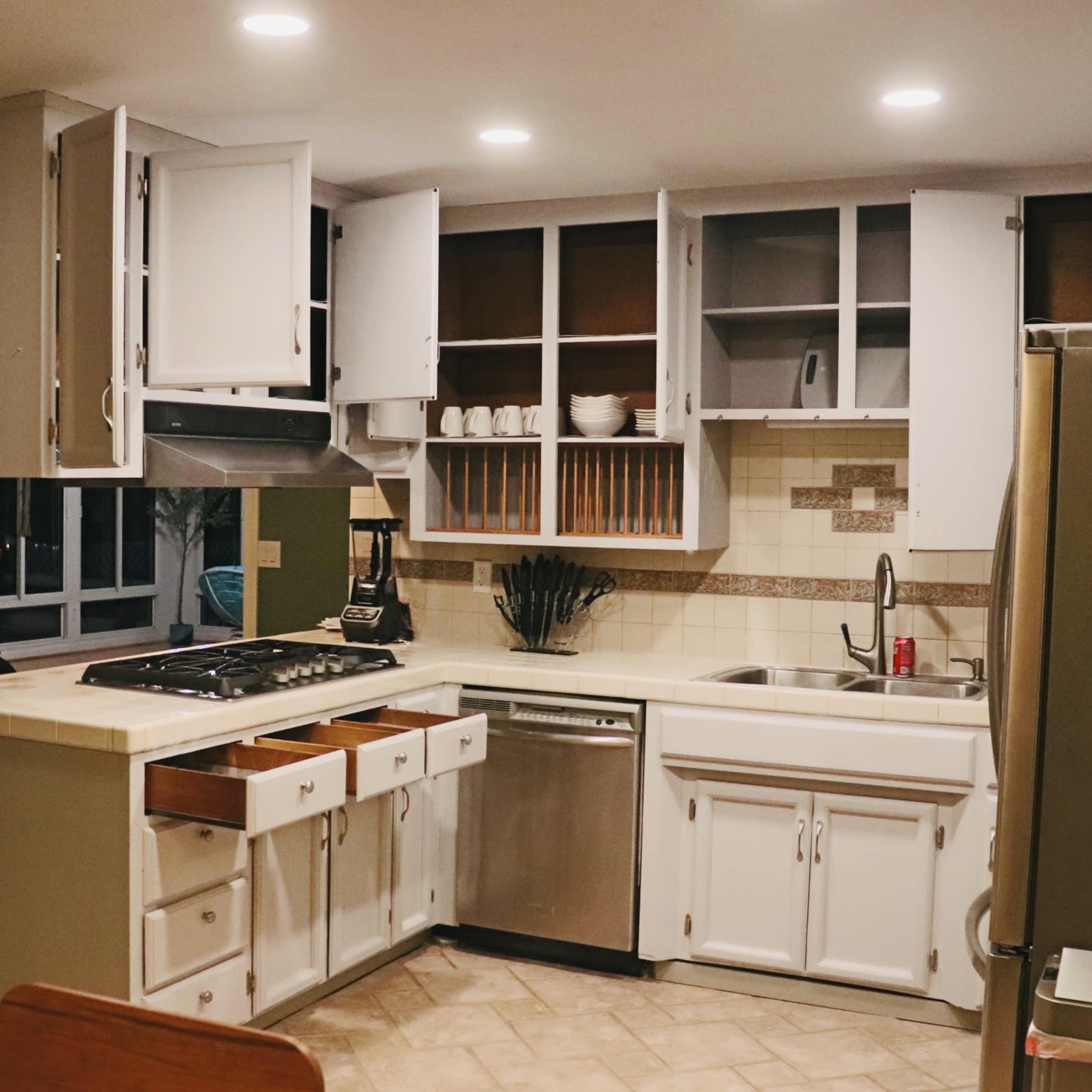 The kitchen features white cabinetry, a stainless steel sink, and a gas stove, with open shelves displaying dishes.