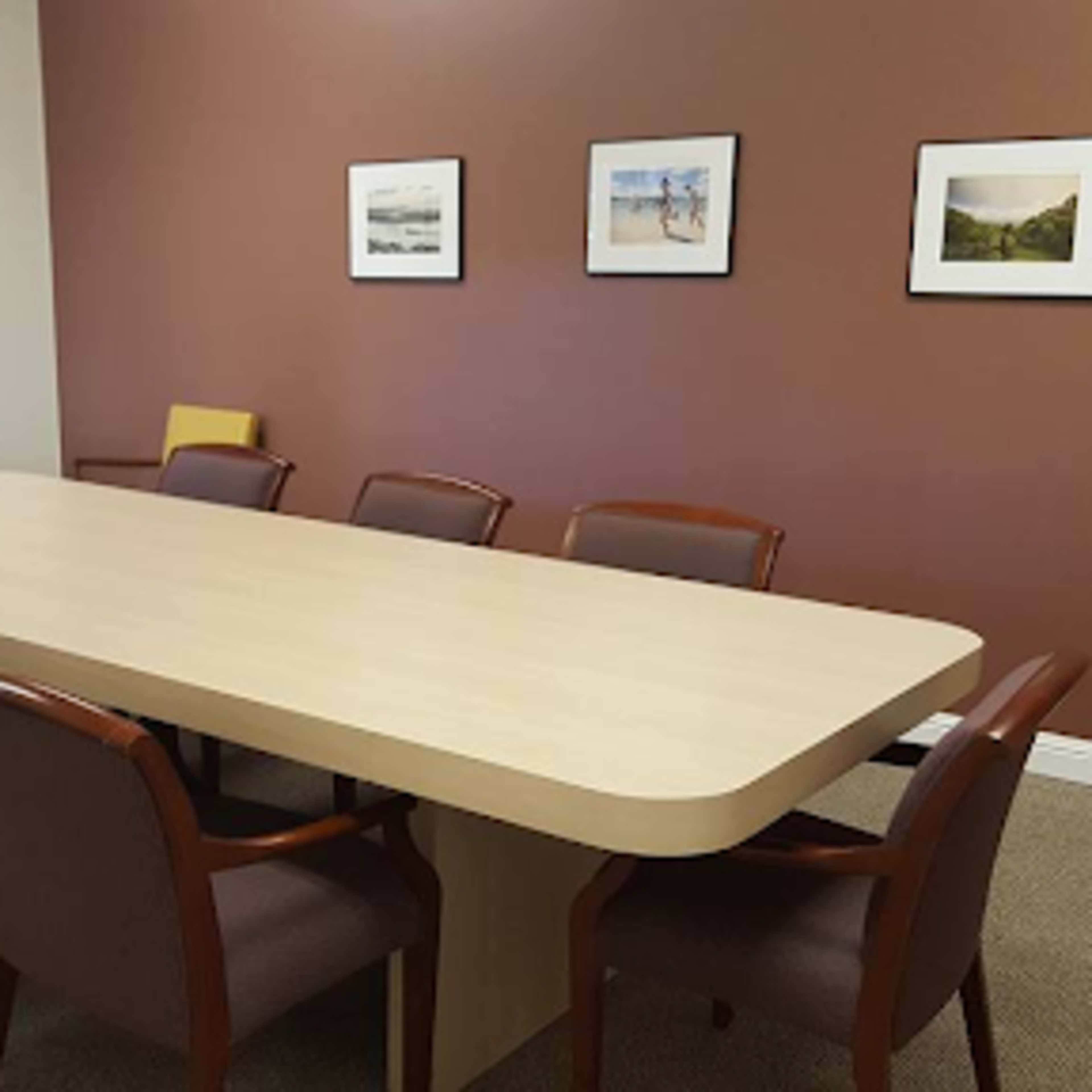 A long wooden table is surrounded by chairs in a meeting room with framed photographs on the walls.