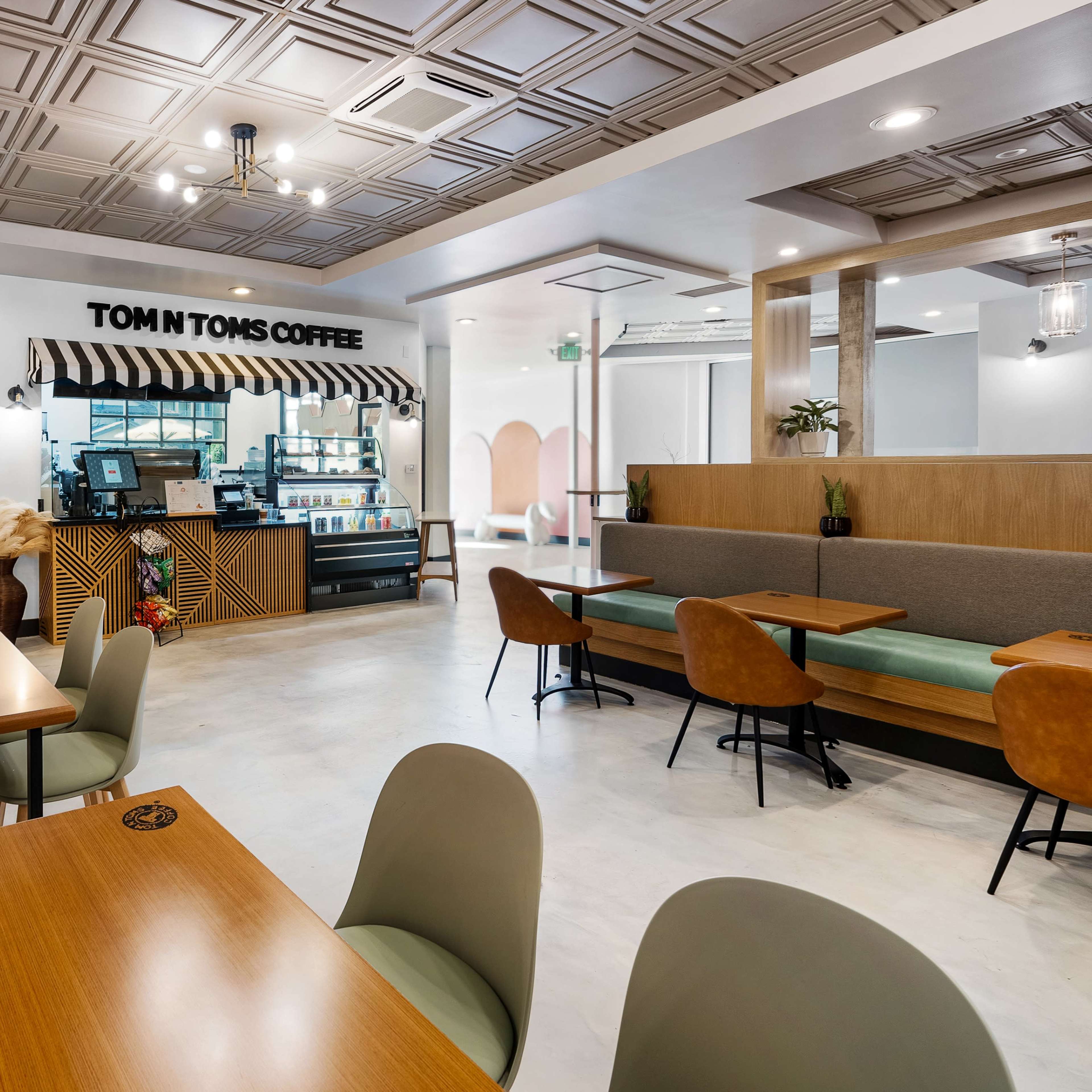 The interior of a coffee shop features wooden tables, green and brown seating, and a service counter with a striped awning.