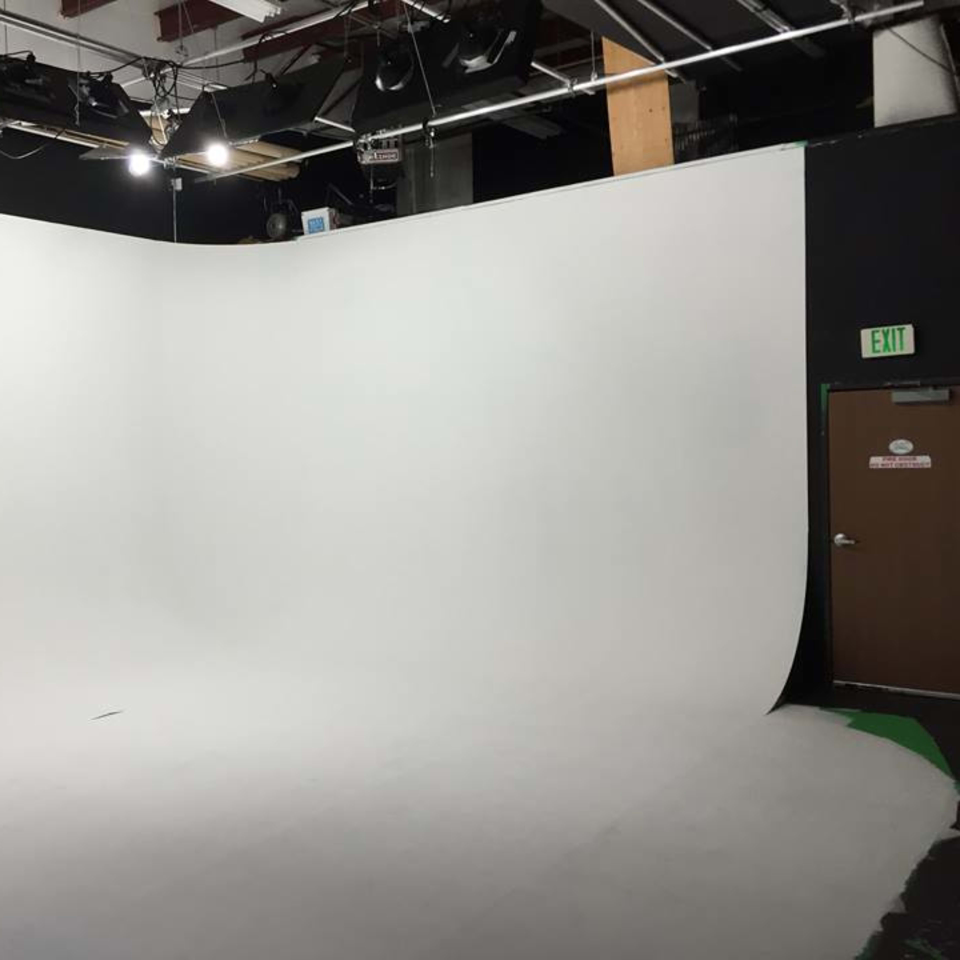 A photography studio featuring a seamless white backdrop and various overhead lights.