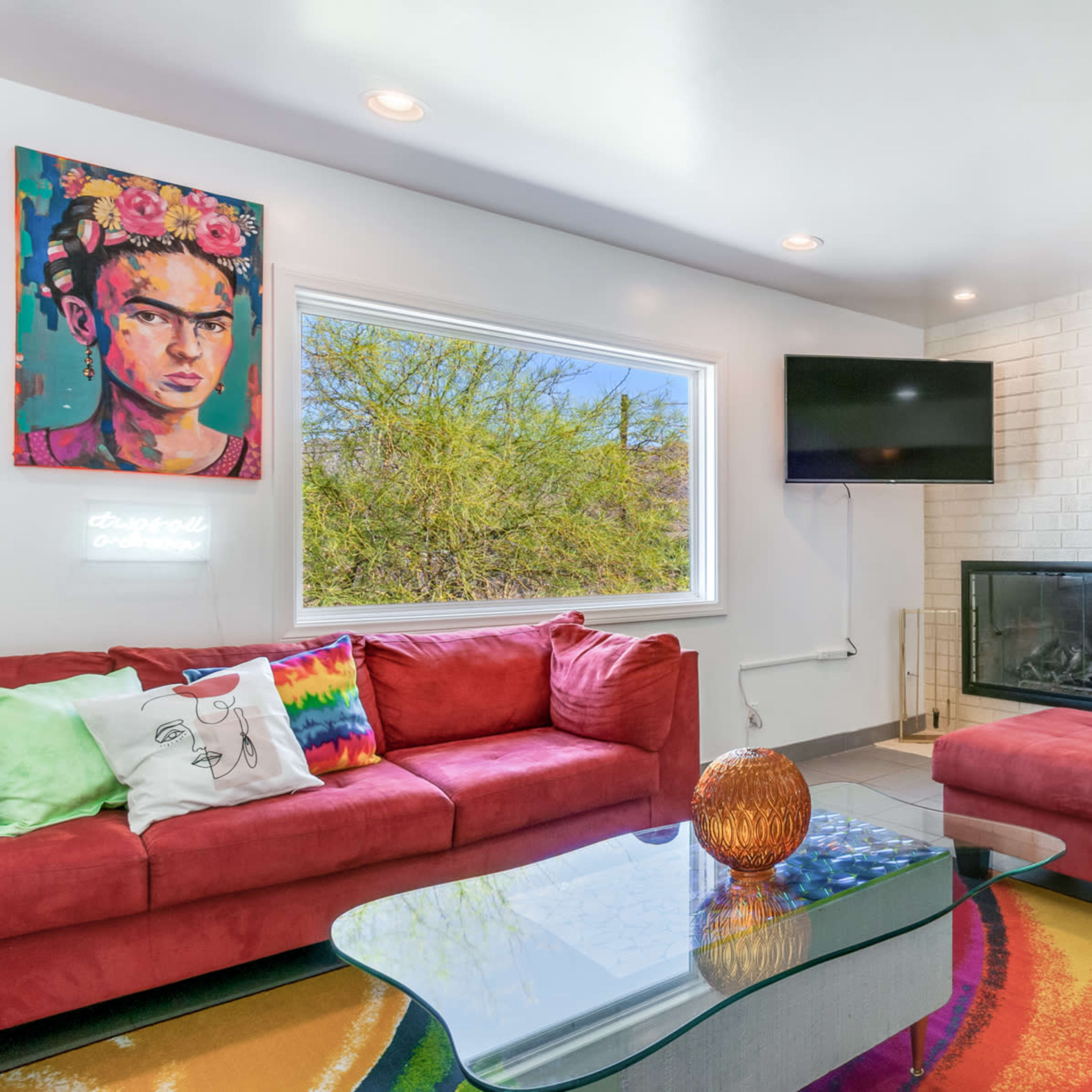 The living area features a red sectional sofa, a glass coffee table, and a wall-mounted television, with a fireplace and dining area visible in the background.