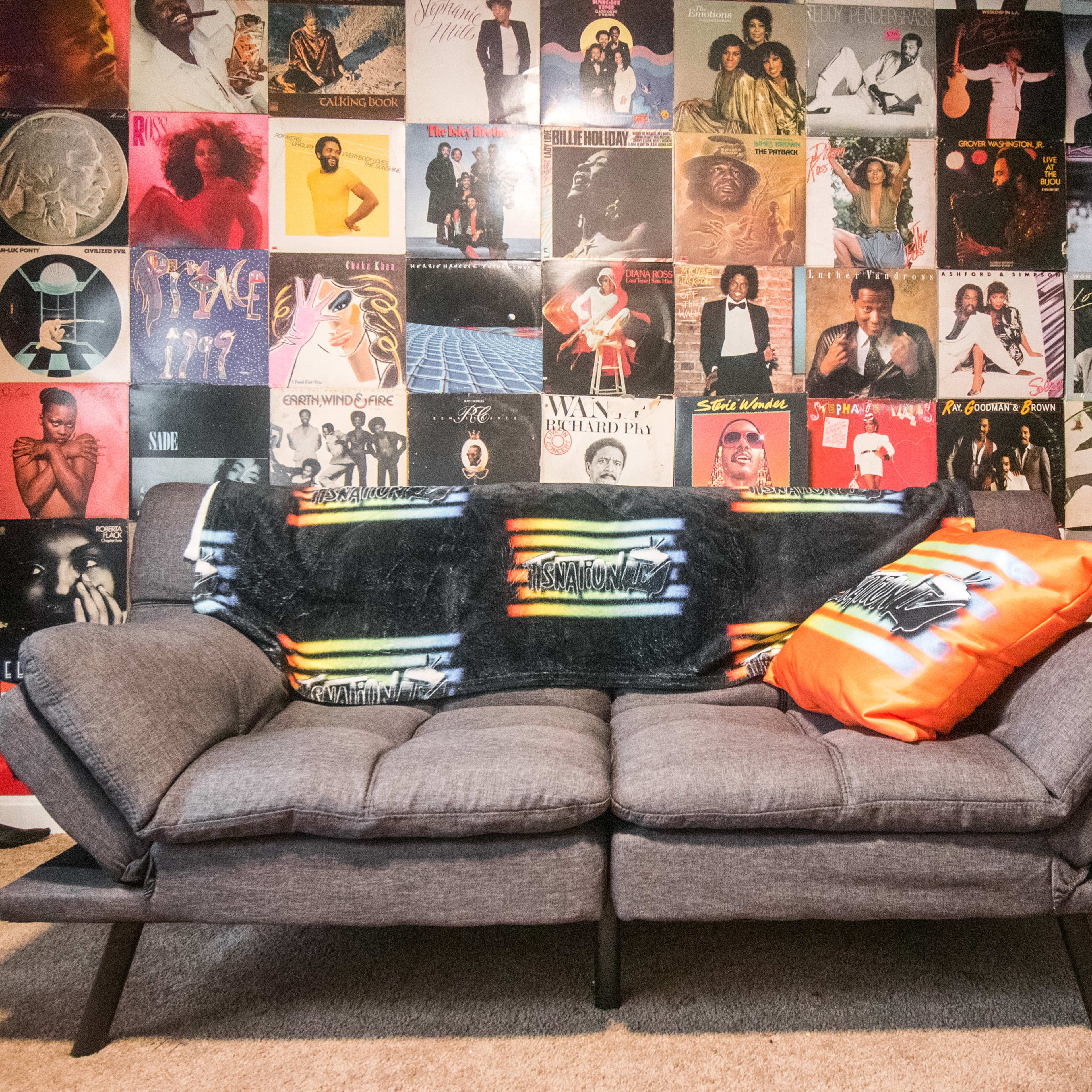 A gray couch with colorful pillows sits in front of a wall covered with vintage album covers.