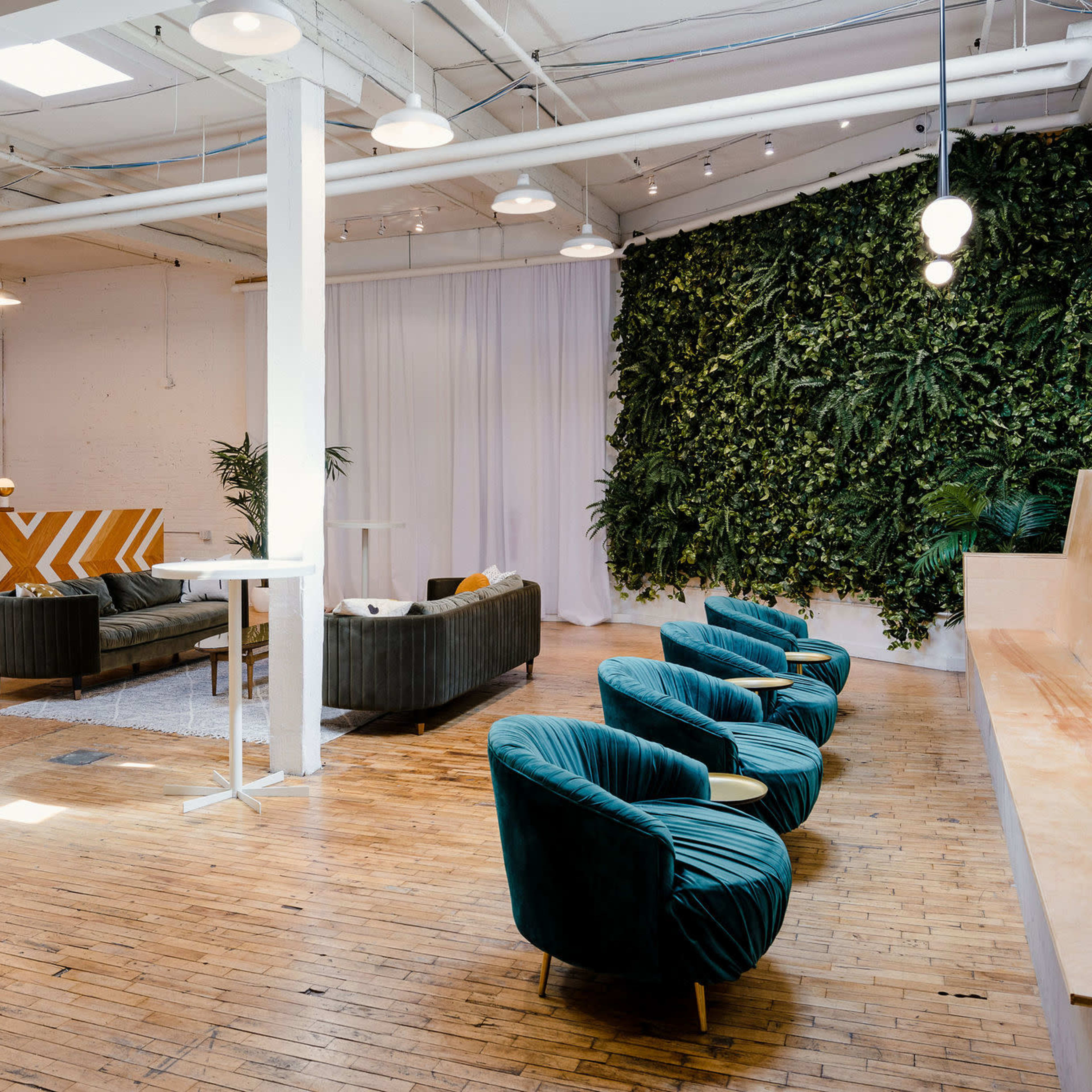 A spacious, modern lounge area with green seating, a vertical plant wall, and wooden floors.