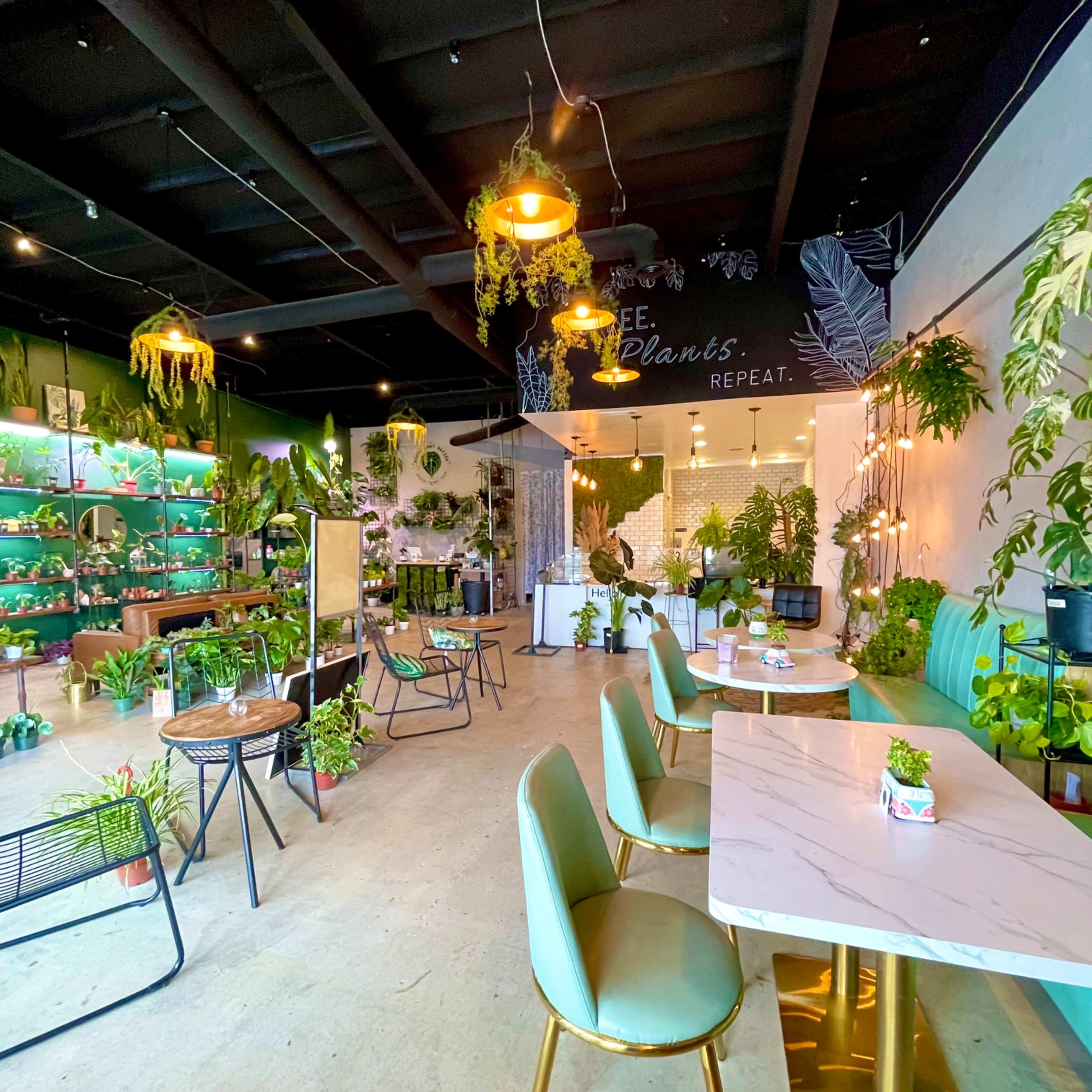 A bright indoor plant shop filled with various potted plants, featuring a seating area with green chairs and a marble table.