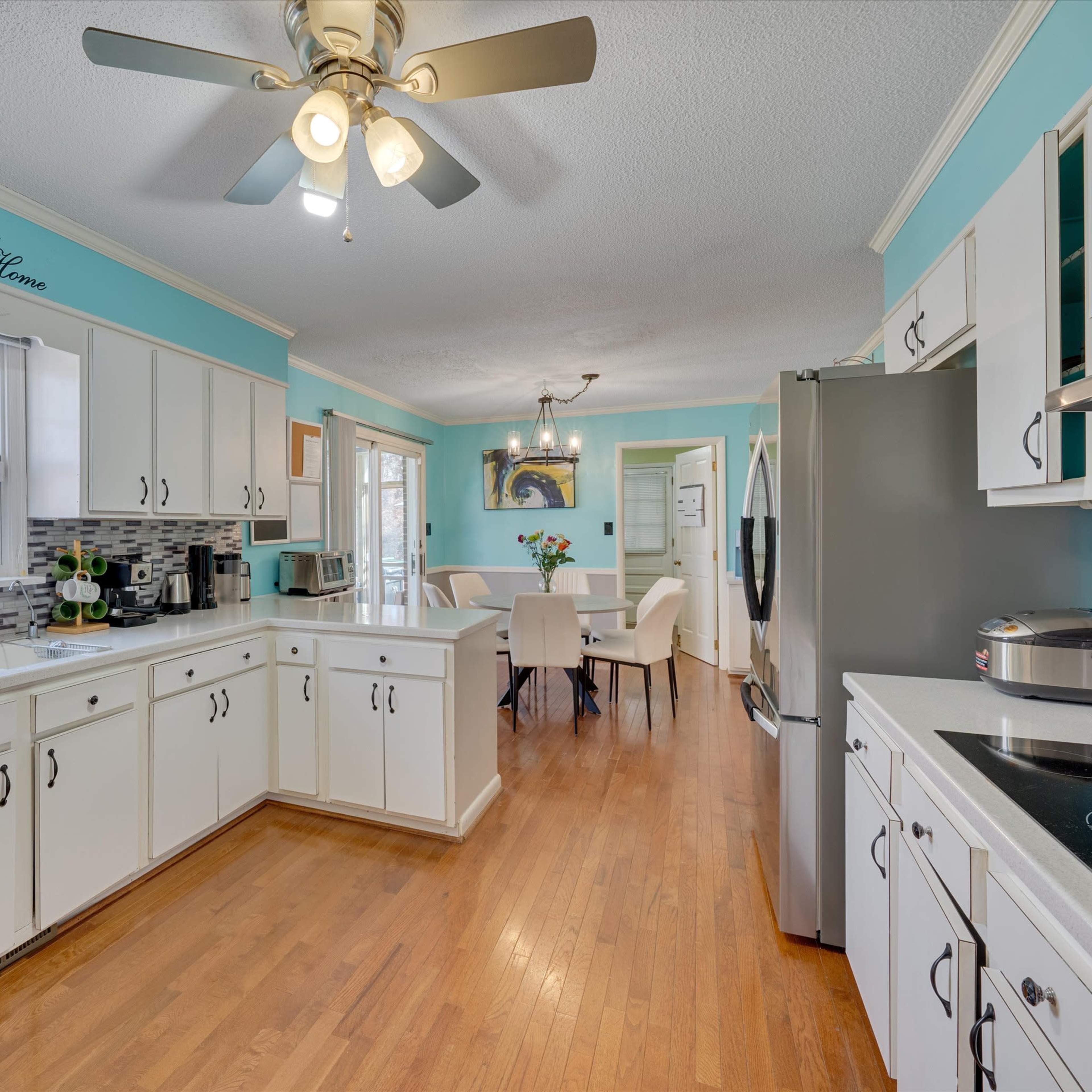 A bright kitchen features white cabinetry, stainless steel appliances, and a view into a dining area with a table and chairs.
