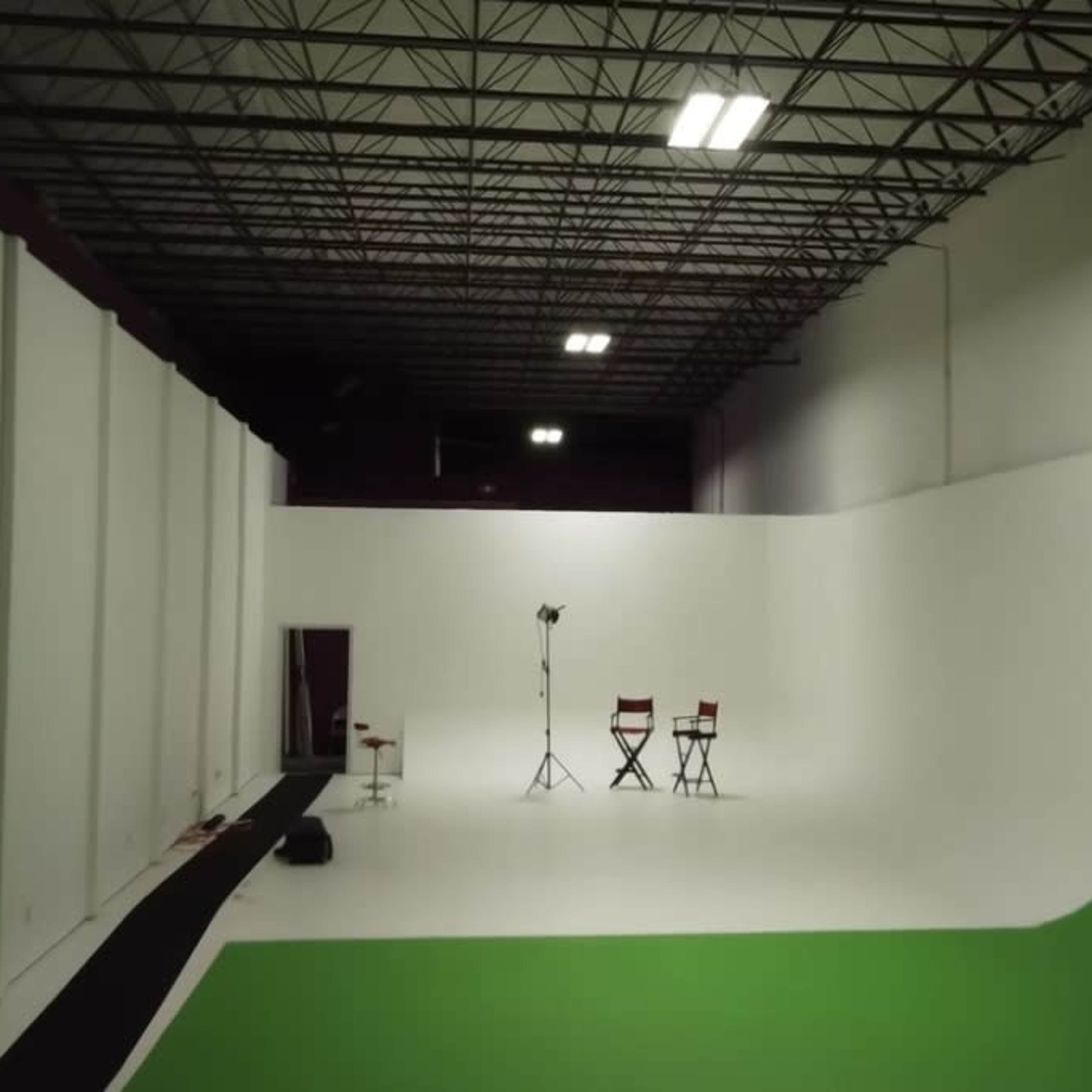 A spacious studio with a green screen backdrop, two director's chairs, and a lighting setup in a well-lit environment.