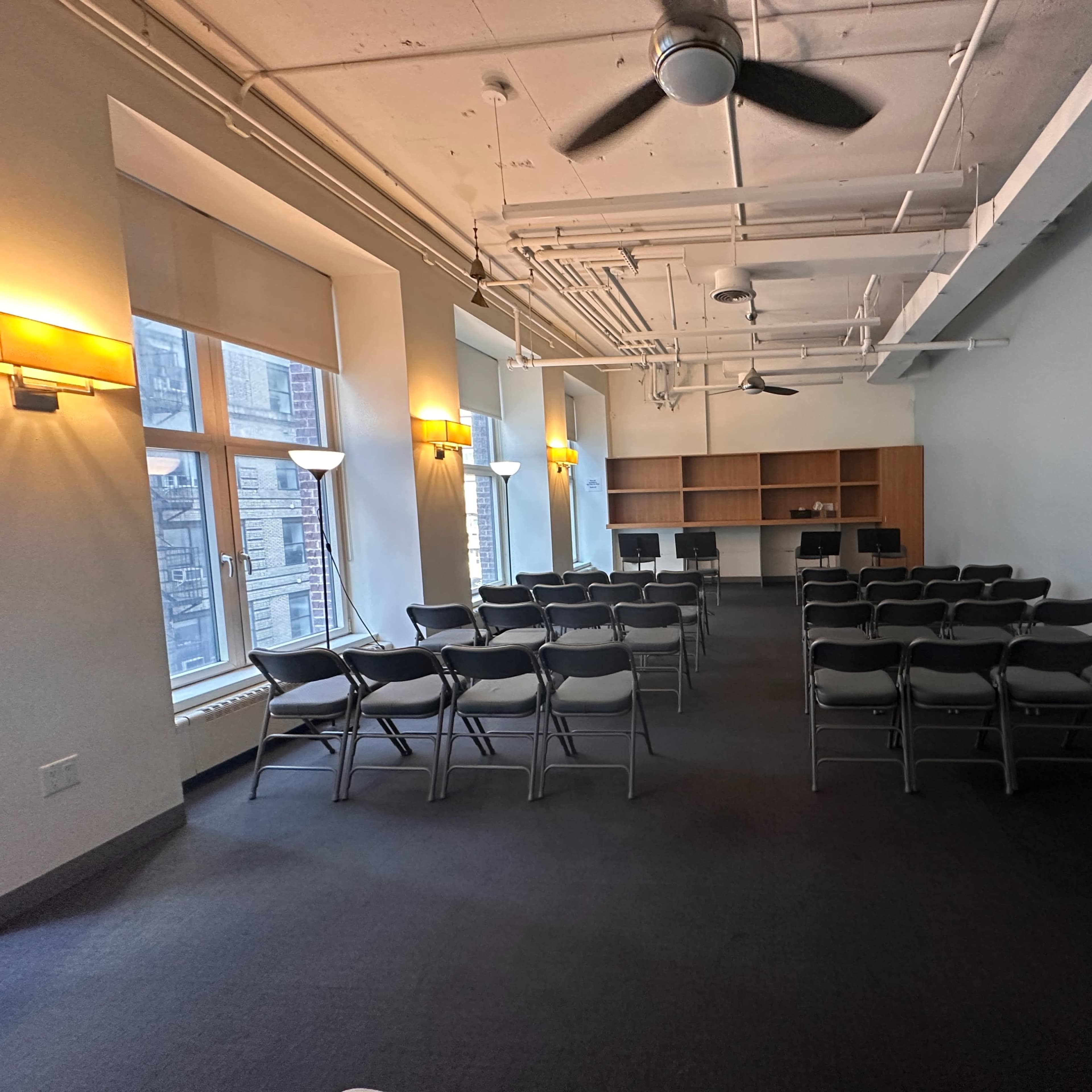 A meeting room features rows of chairs facing a counter area, illuminated by natural light from large windows.