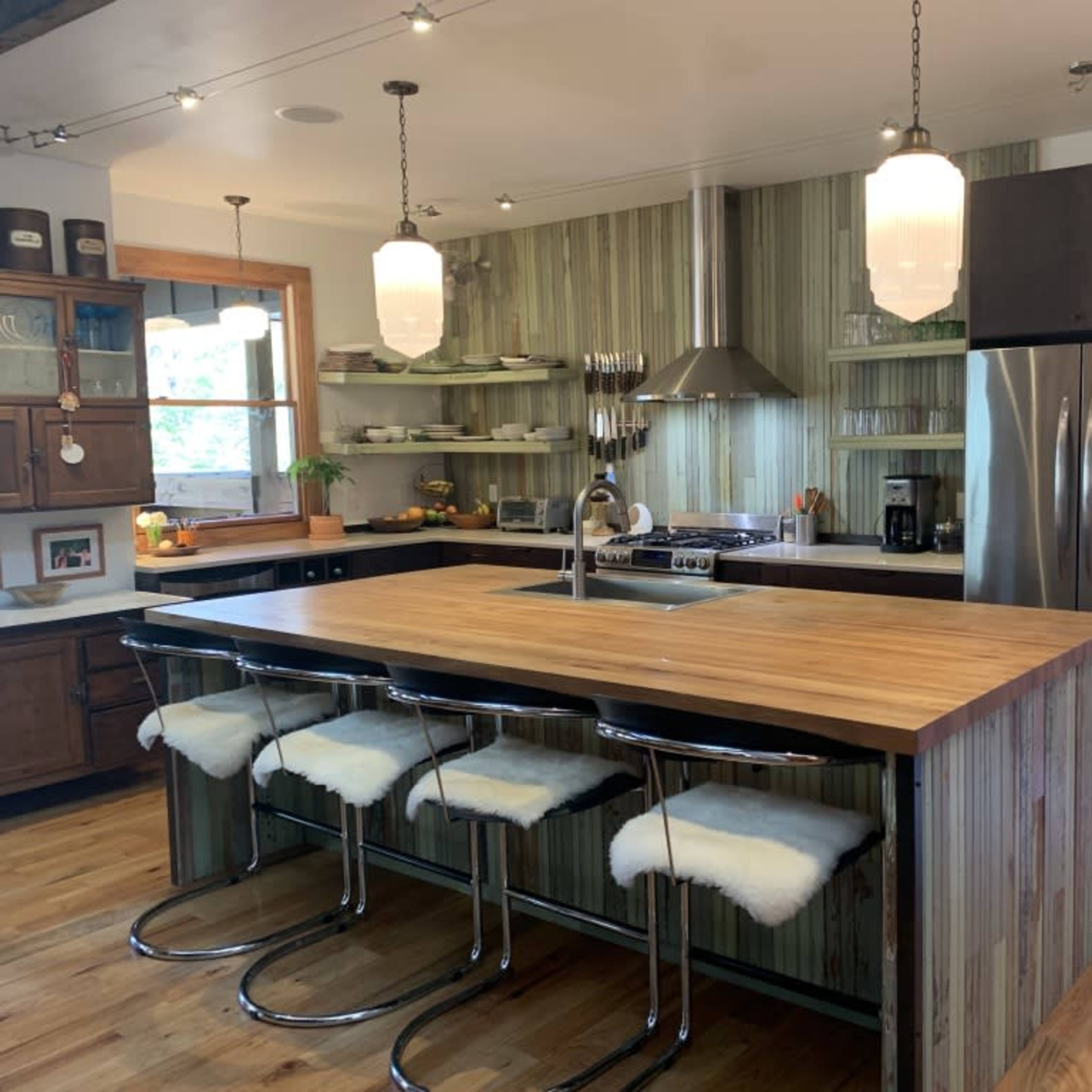 A modern kitchen featuring a wooden island with bar stools, stainless steel appliances, and green wall panels.