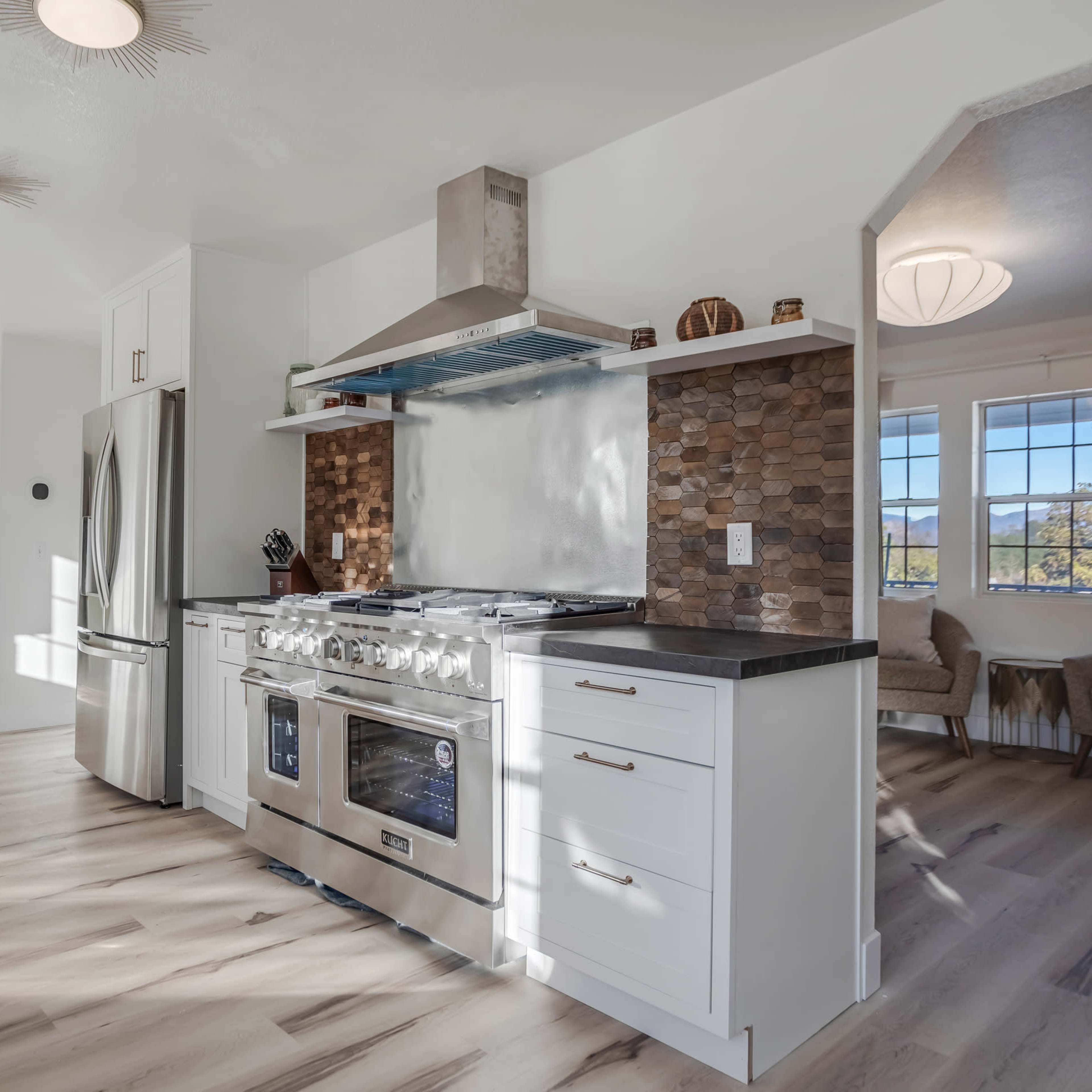 A modern kitchen features stainless steel appliances, a stone backsplash, and light wood flooring.