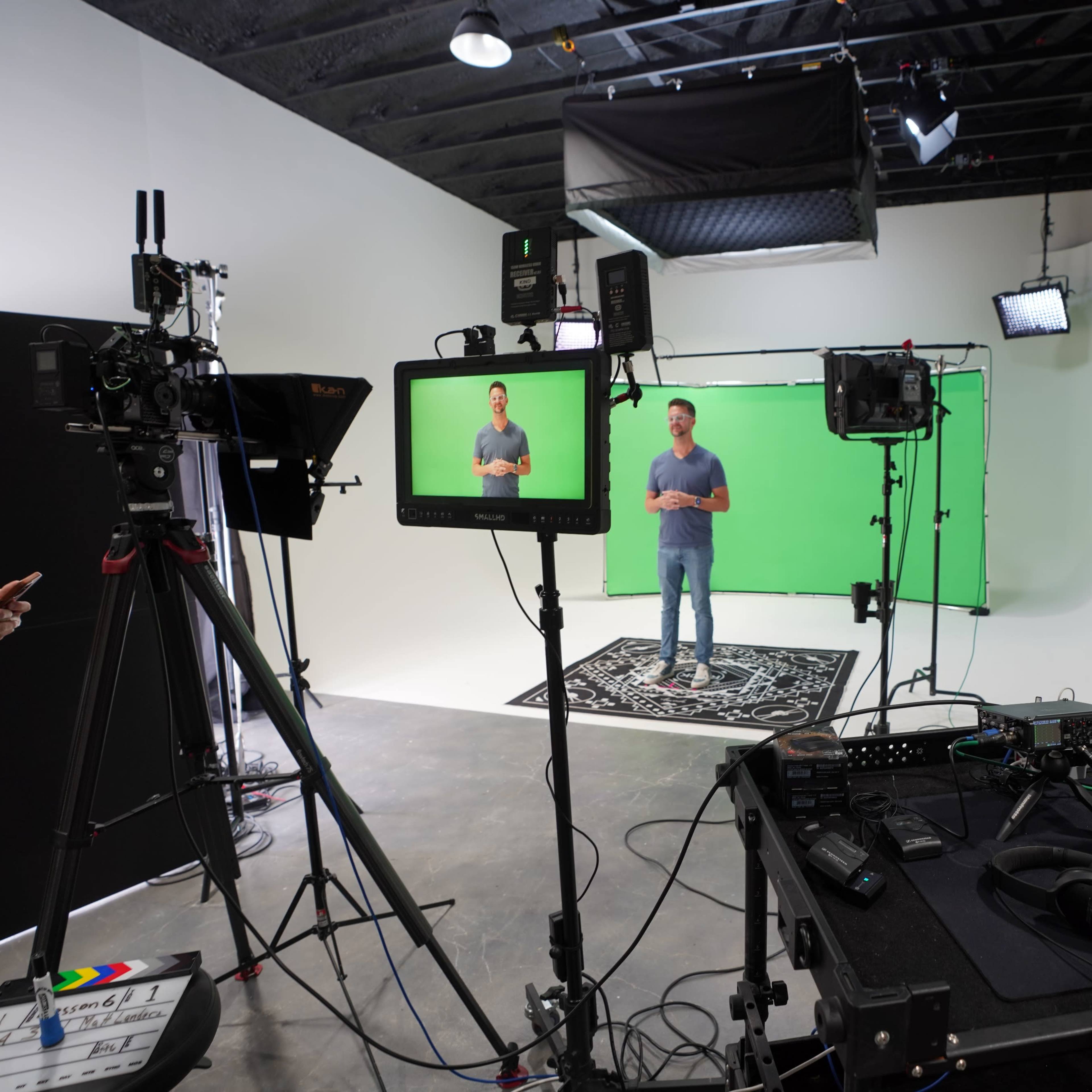 A person stands in front of a green screen, surrounded by video equipment and lighting in a studio setting.