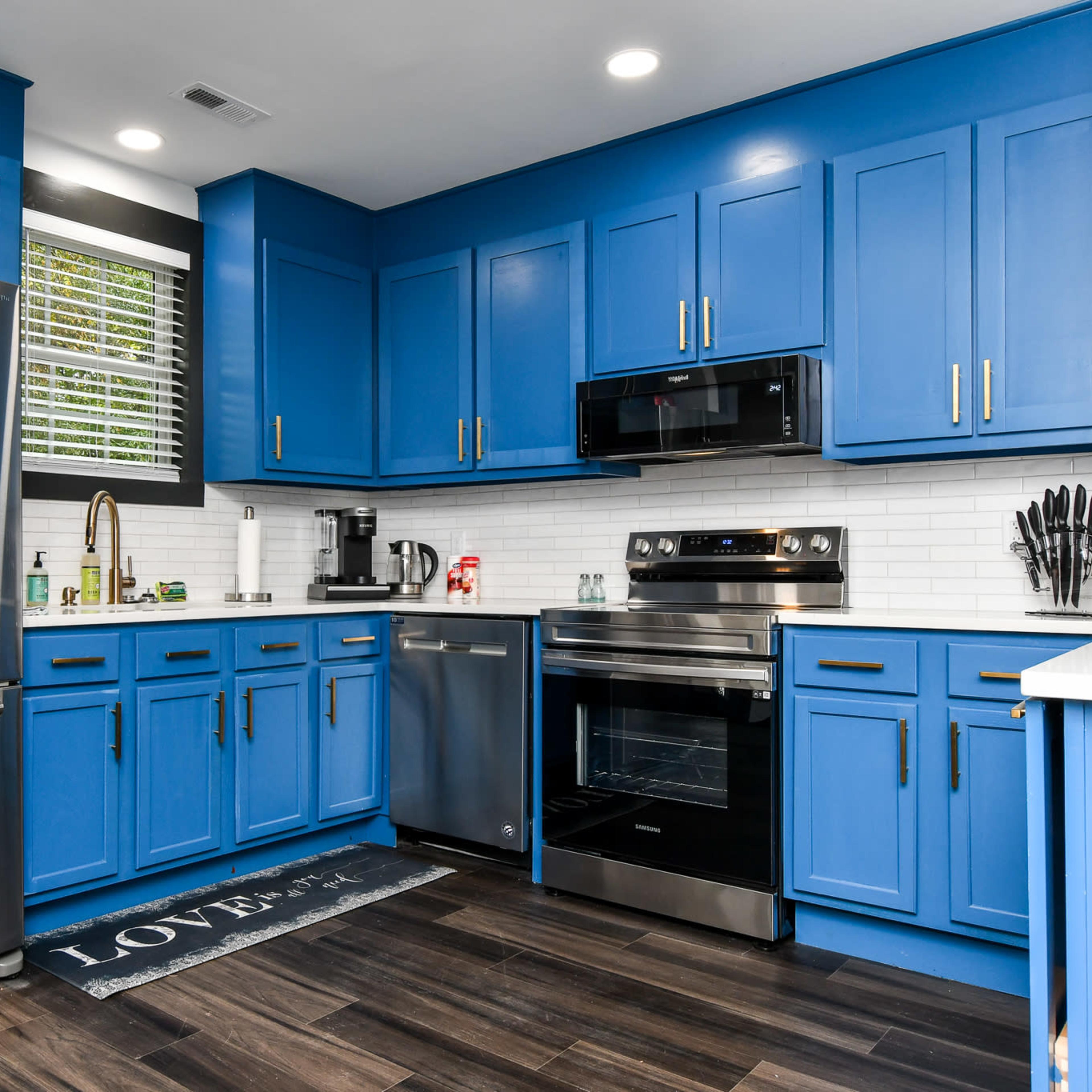 A modern kitchen features blue cabinets, stainless steel appliances, a white backsplash, and a dark wood floor.