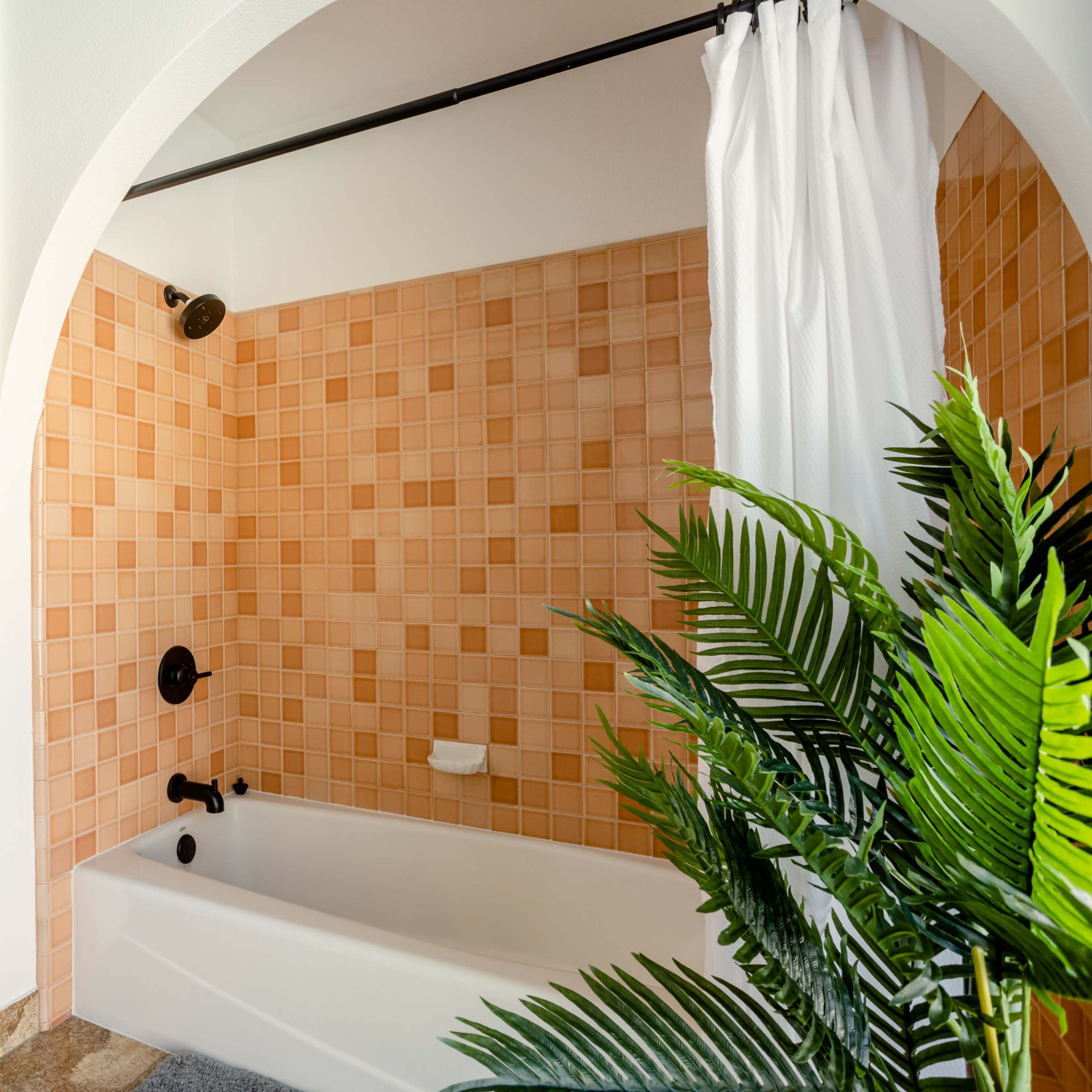 A bathroom with a bathtub enclosed by a tiled wall, a shower curtain, and a potted plant in the foreground.