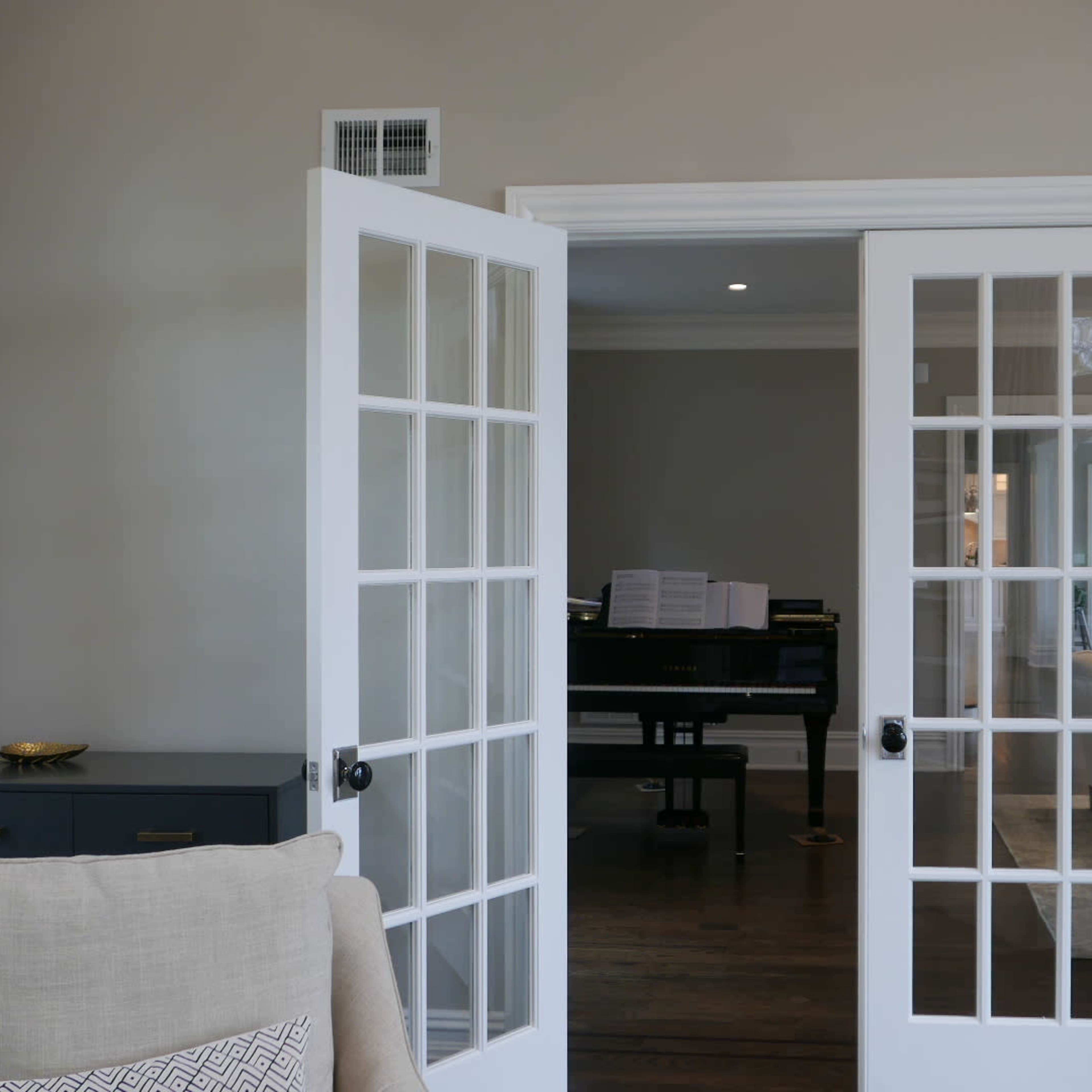 A pair of French doors leading into a room with a grand piano visible in the background.