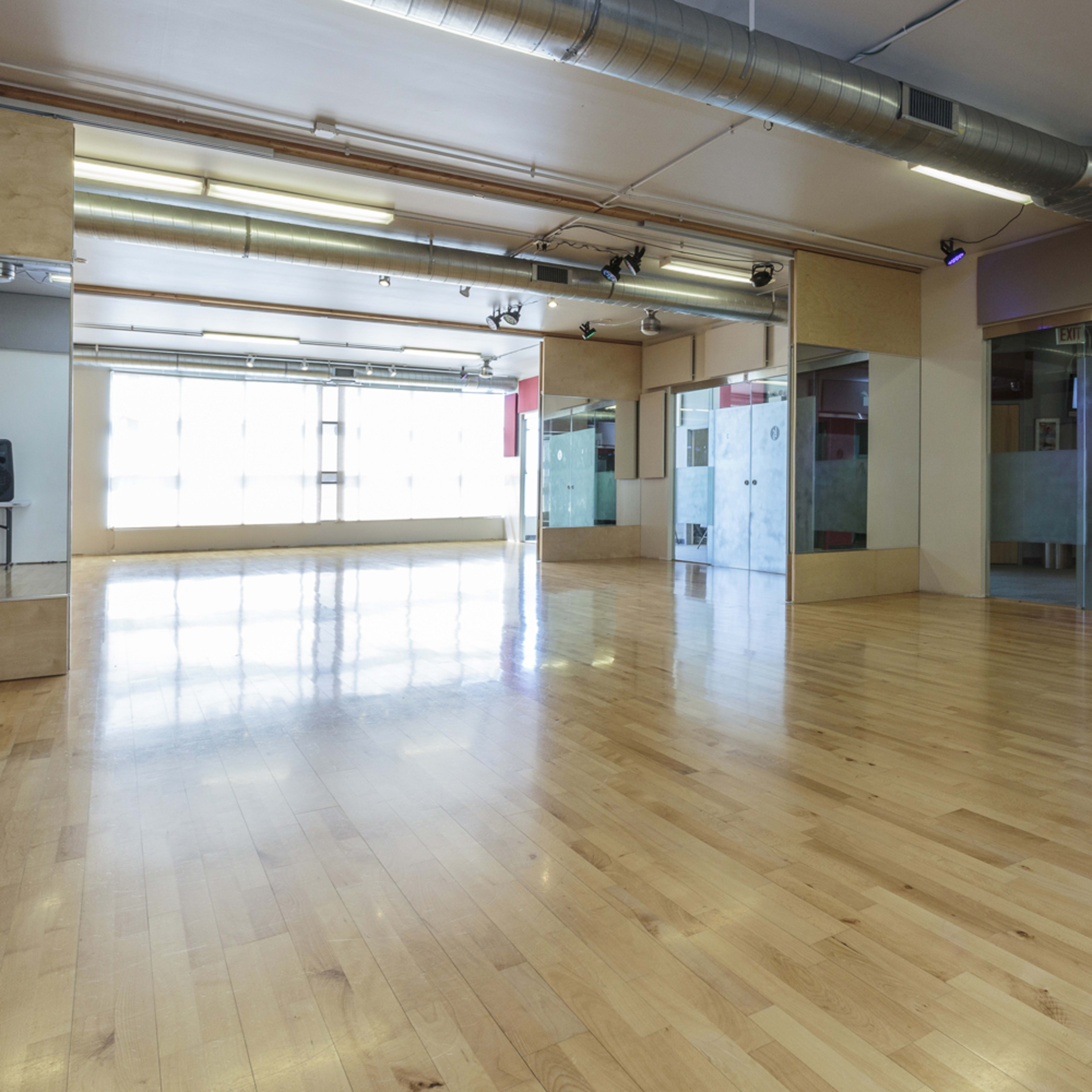 A spacious dance studio with hardwood floors, large mirrors on the walls, and glass-paneled doors.
