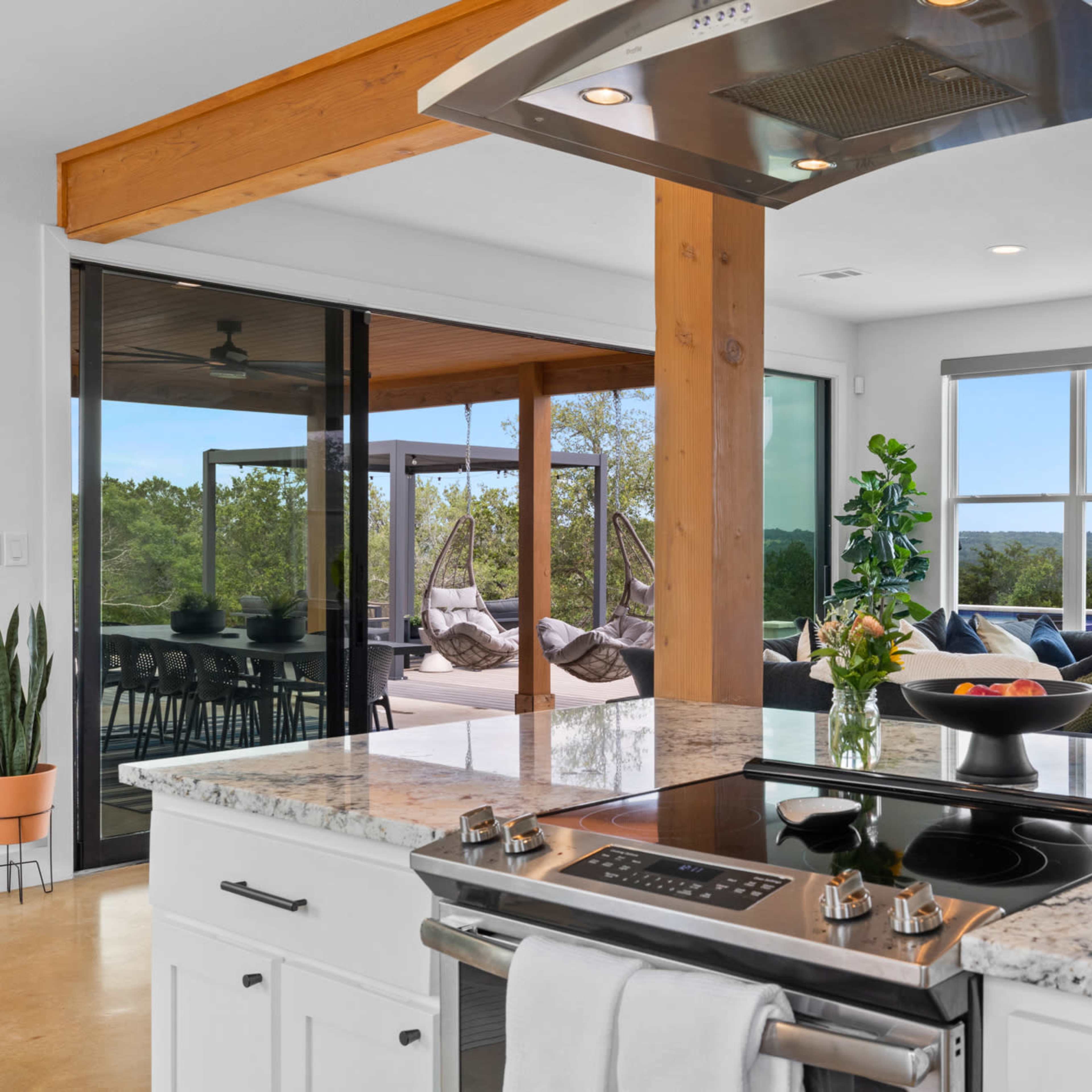 A modern kitchen with a granite countertop features a stove and an open view to a living area and outdoor patio.