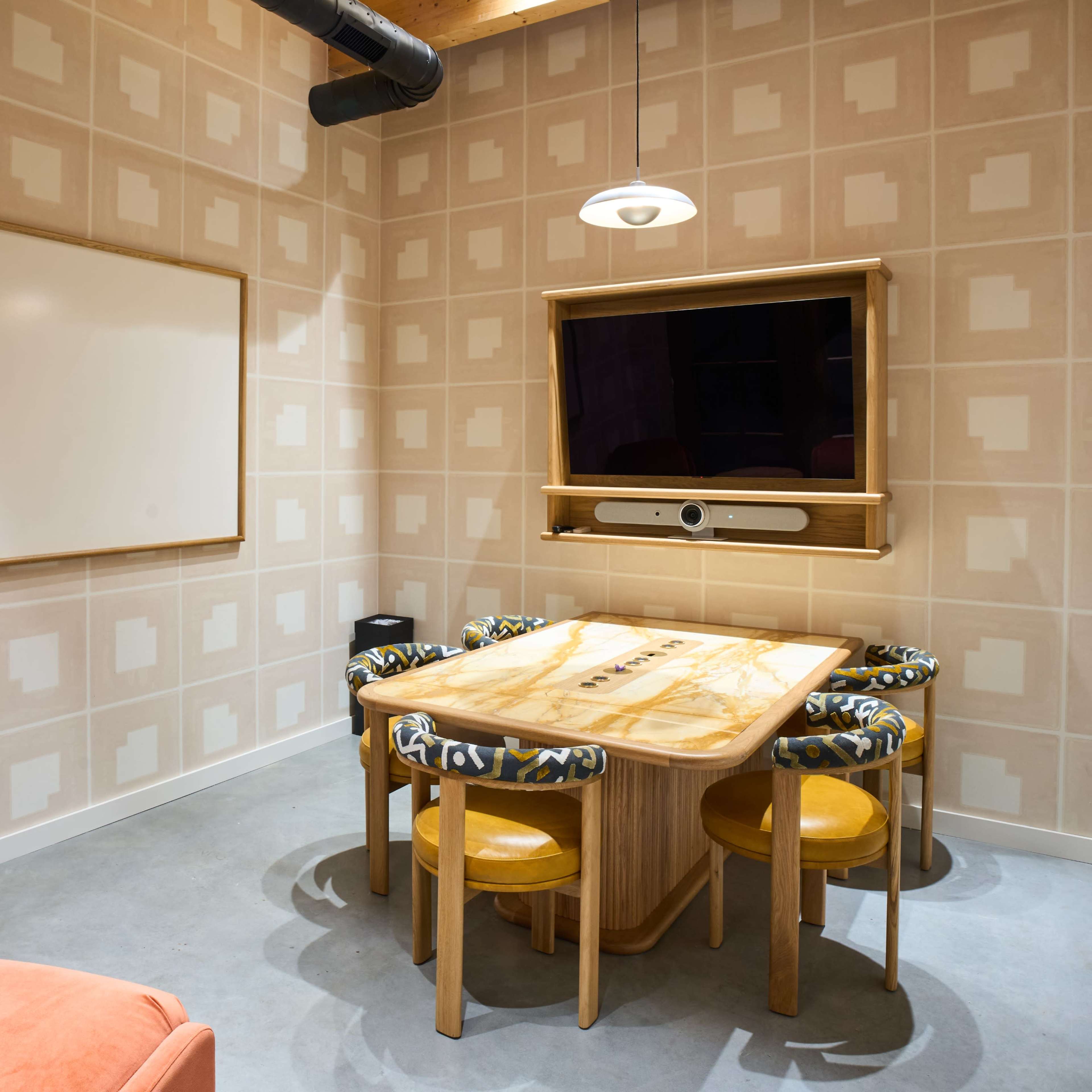 A conference room features a wooden table surrounded by six chairs, a whiteboard on one wall, and a mounted television on another.