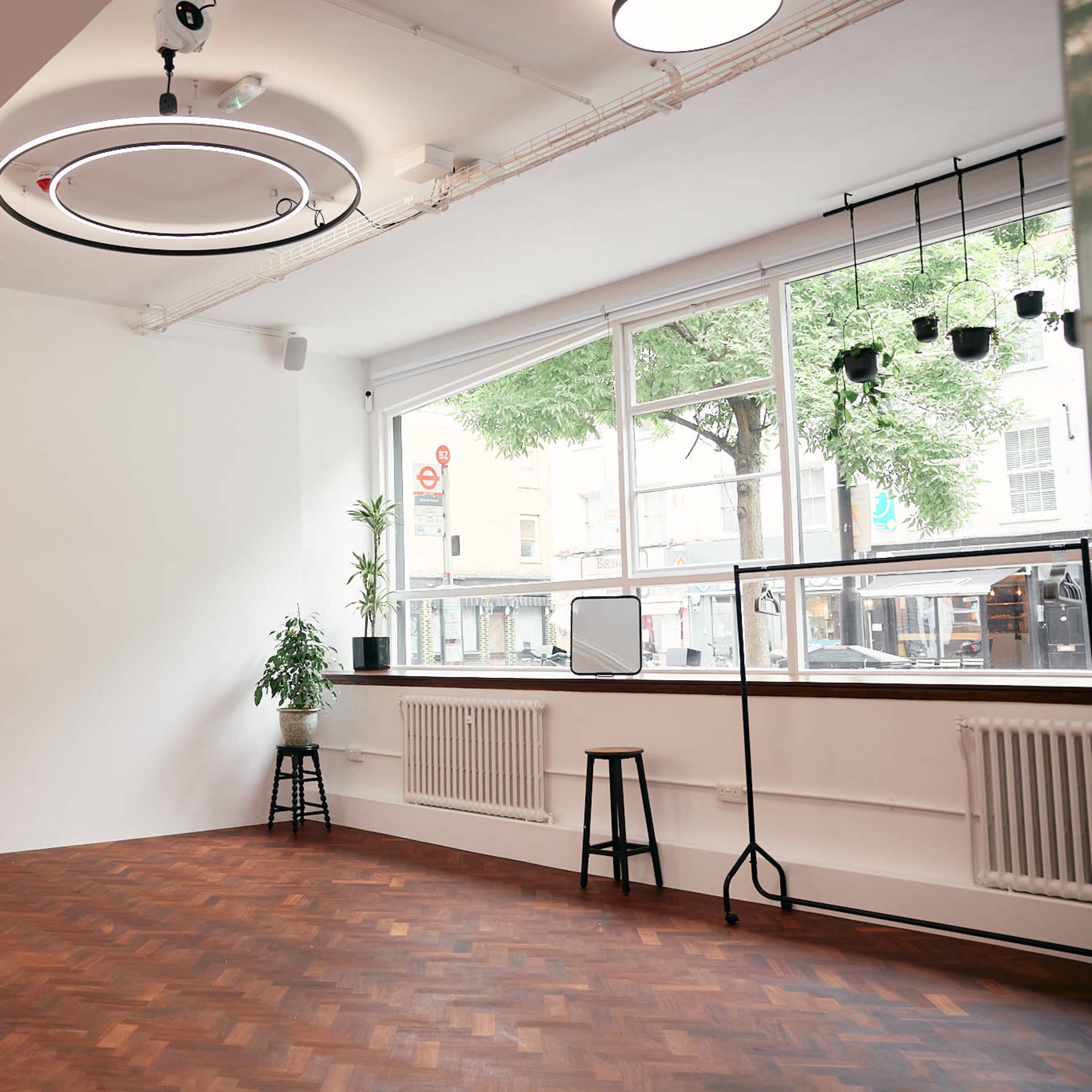A sparsely decorated room with hardwood flooring, a large window letting in natural light, and a few stools arranged near the window.