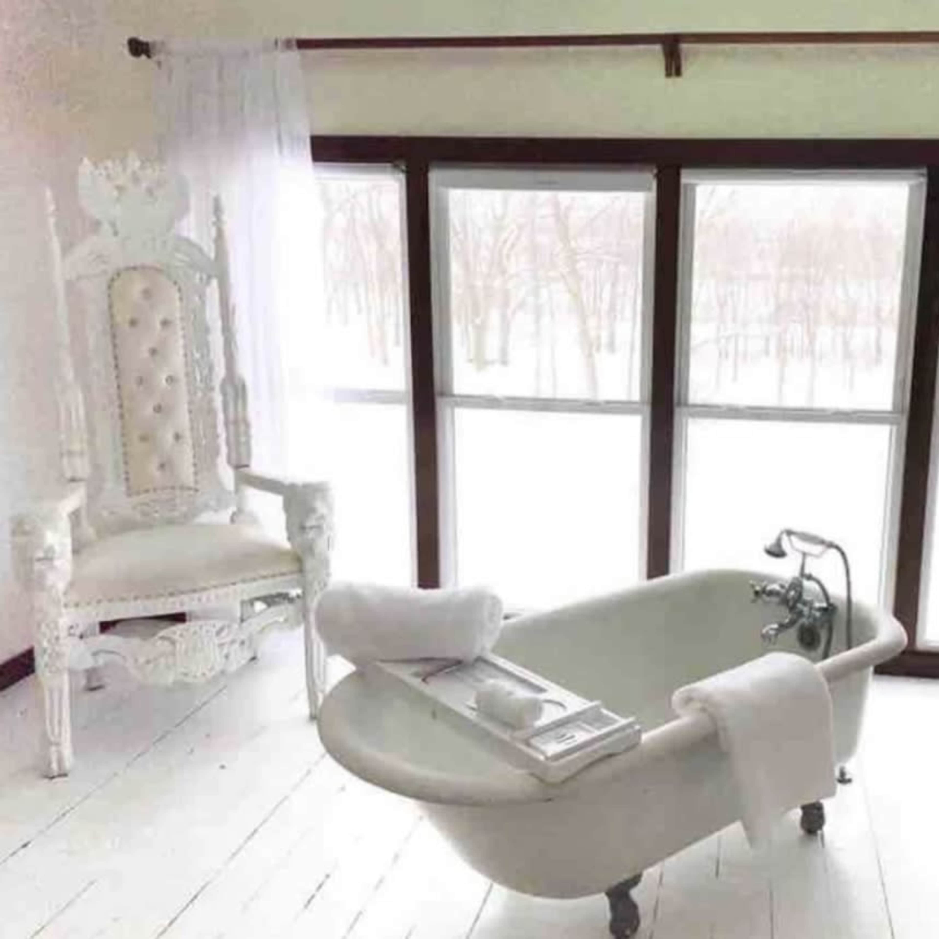 A vintage bathtub is positioned in a bright room with large windows offering a view of a snowy landscape.
