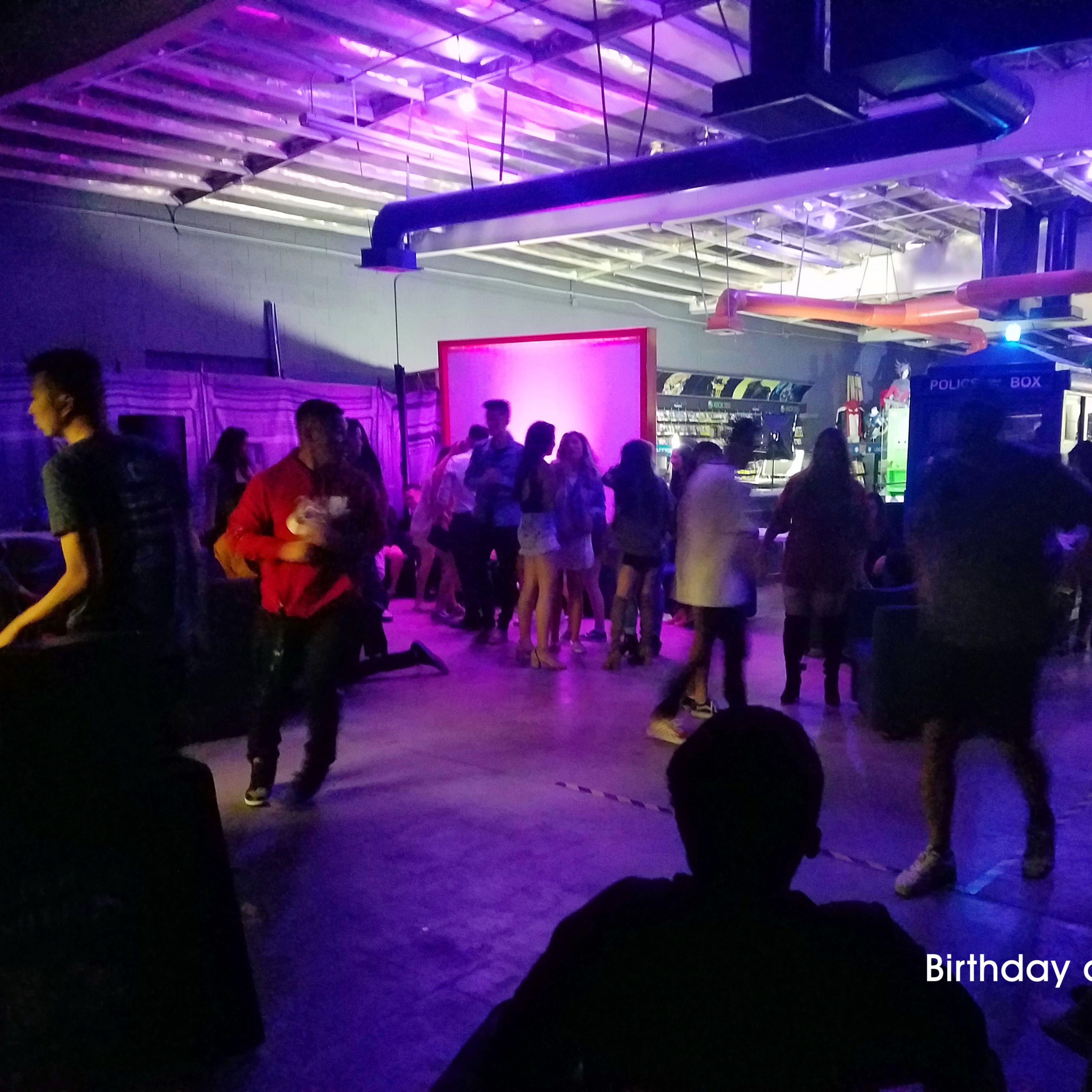 A crowd of people mingles and celebrates in a dimly lit venue with purple and blue lighting.