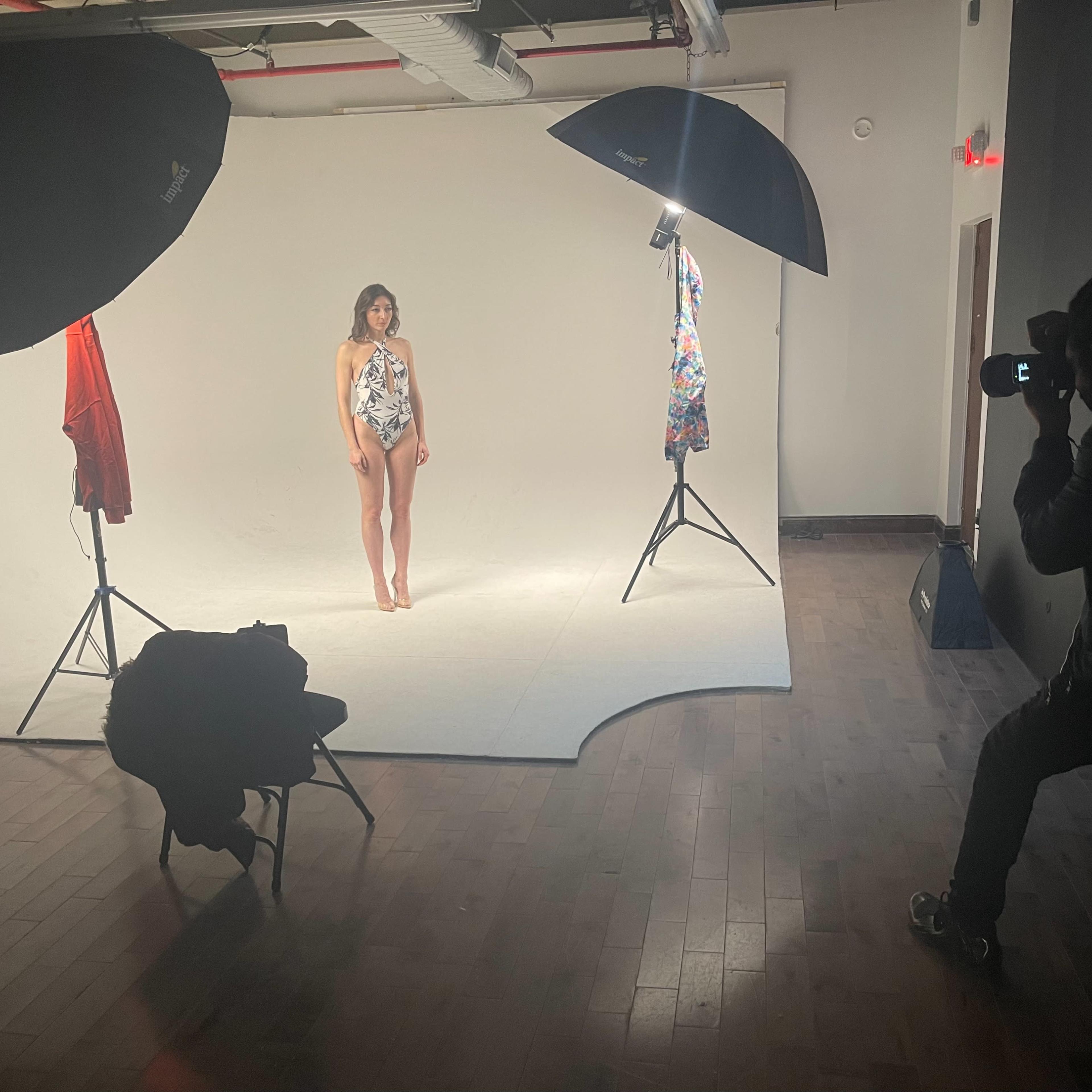 A photographer is capturing images of a model wearing a swimsuit in a studio setting with softbox lighting.