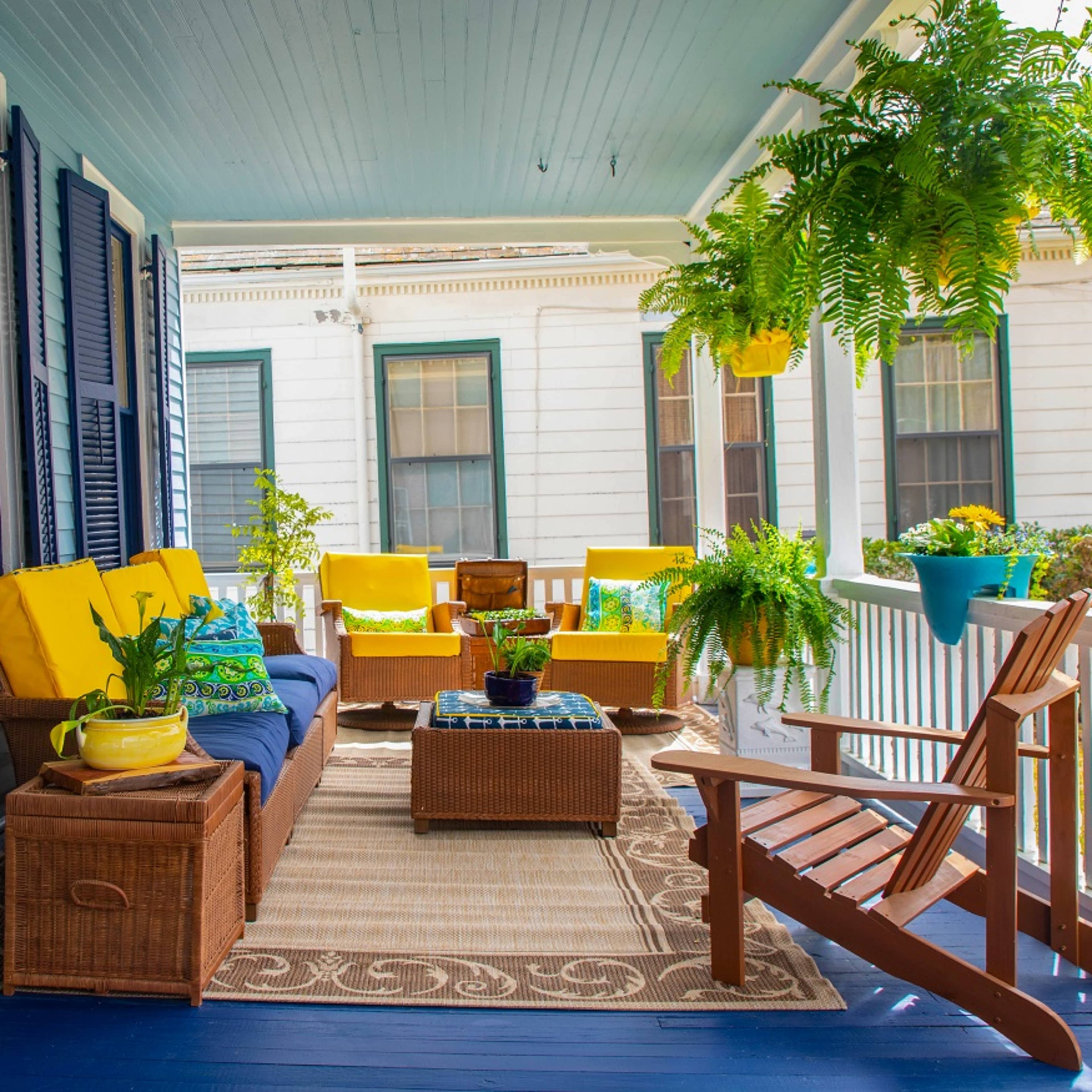 A porch decorated with yellow cushions, a brown wicker seating arrangement, and various houseplants.
